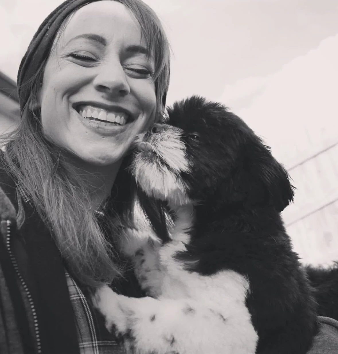 A woman smiling as a puppy licks her face.