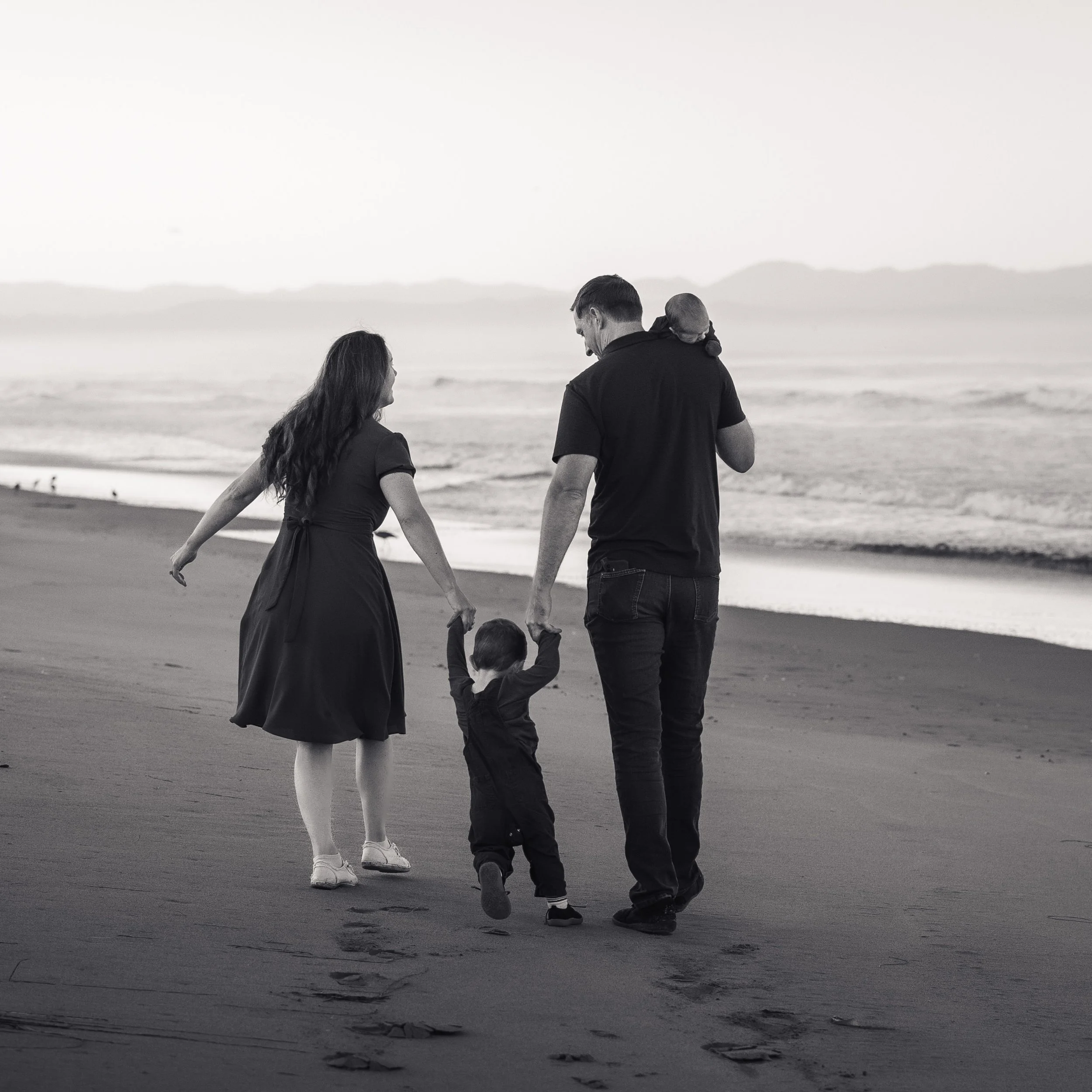 Family walks along the beach together, holding hands.