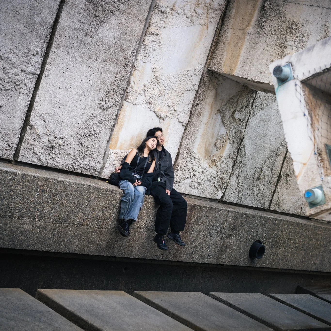 Couple in streetwear sit leaning against each other in San Francisco, California.