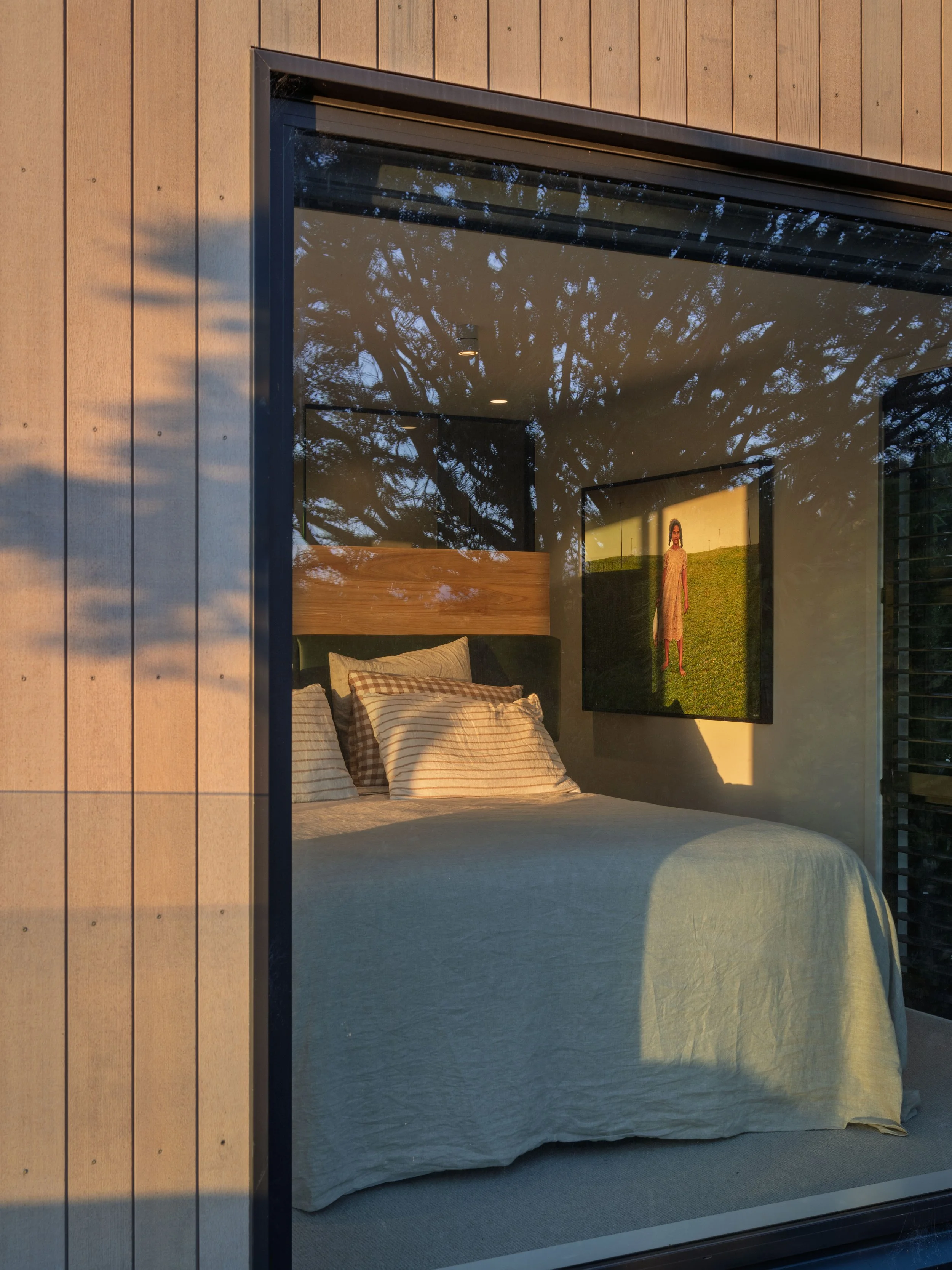 Bedroom with large bed and window reflecting trees outside. There is a picture of a woman on a green background on the wall.