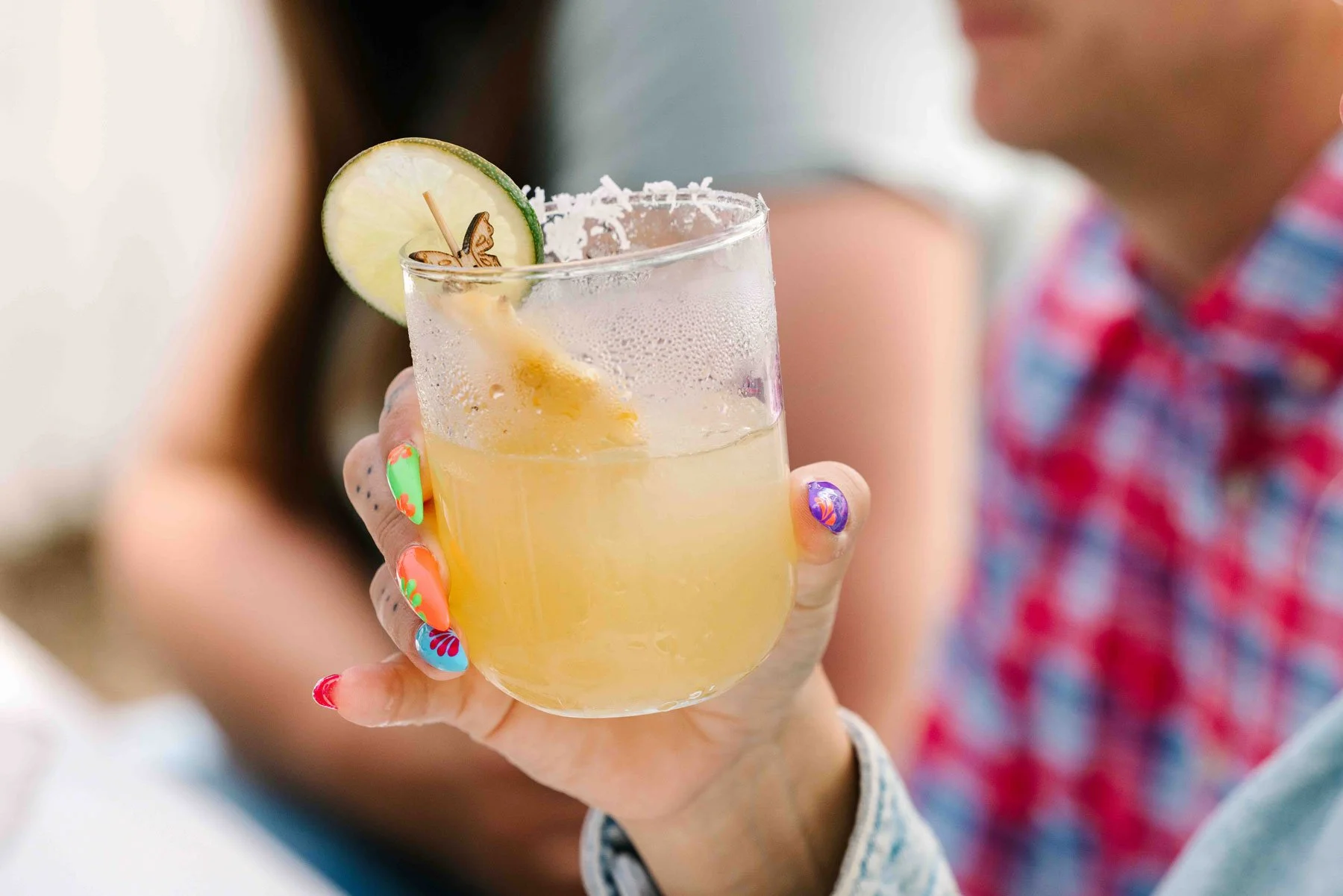 Person holding a glass of yellow margarita with a salted rim, lime wedge, and butterfly decoration