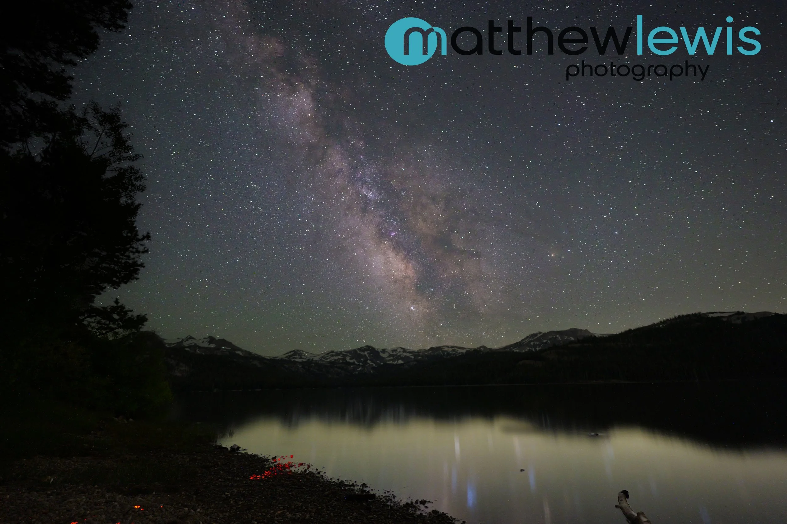Nighttime landscape of Caples Lake, California with a mountain range in the background, starry sky, and the Milky Way galaxy visible overhead.