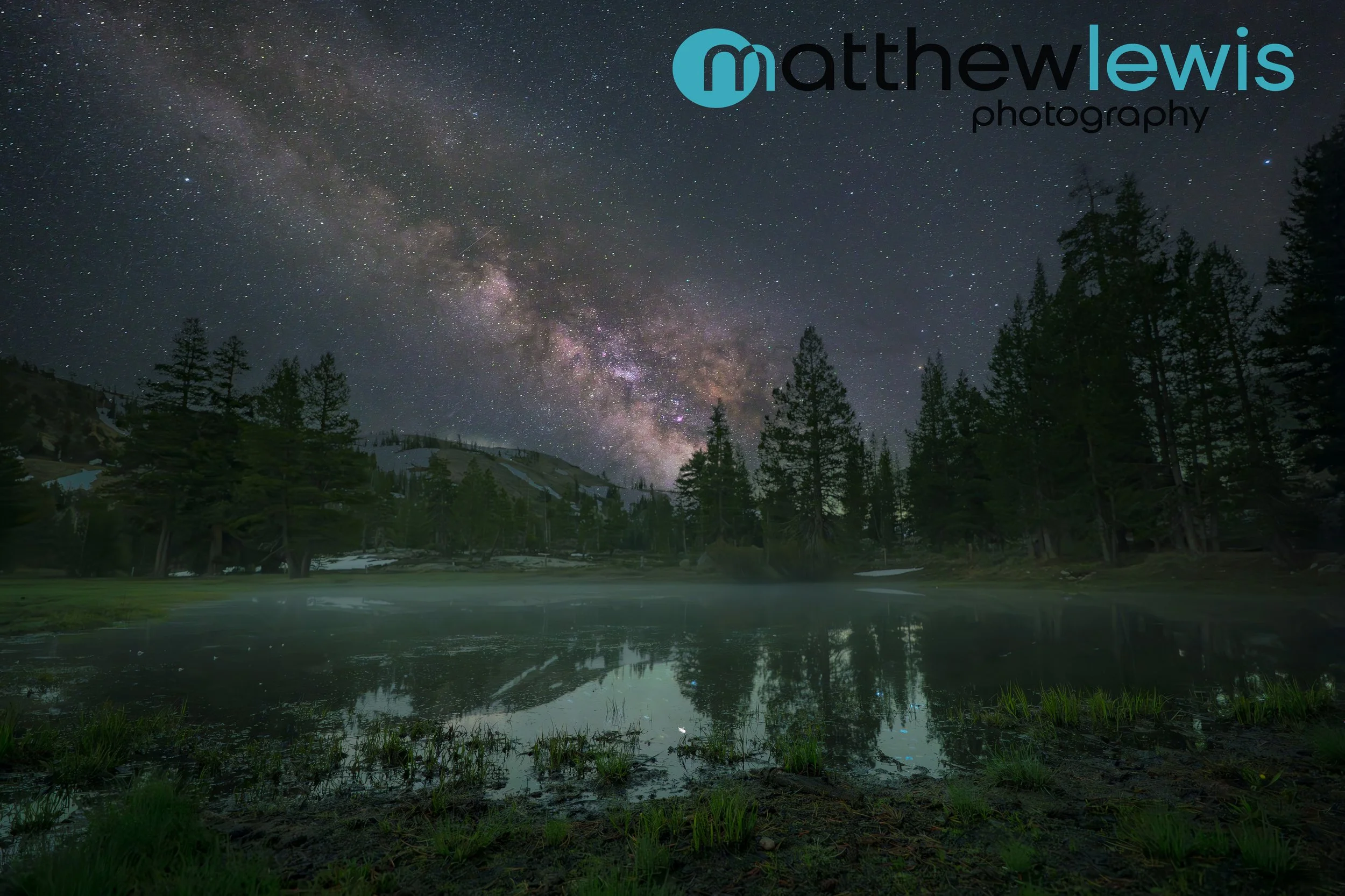 Night sky filled with stars and the Milky Way galaxy over Caples Lake, California surrounded by trees and mountains.