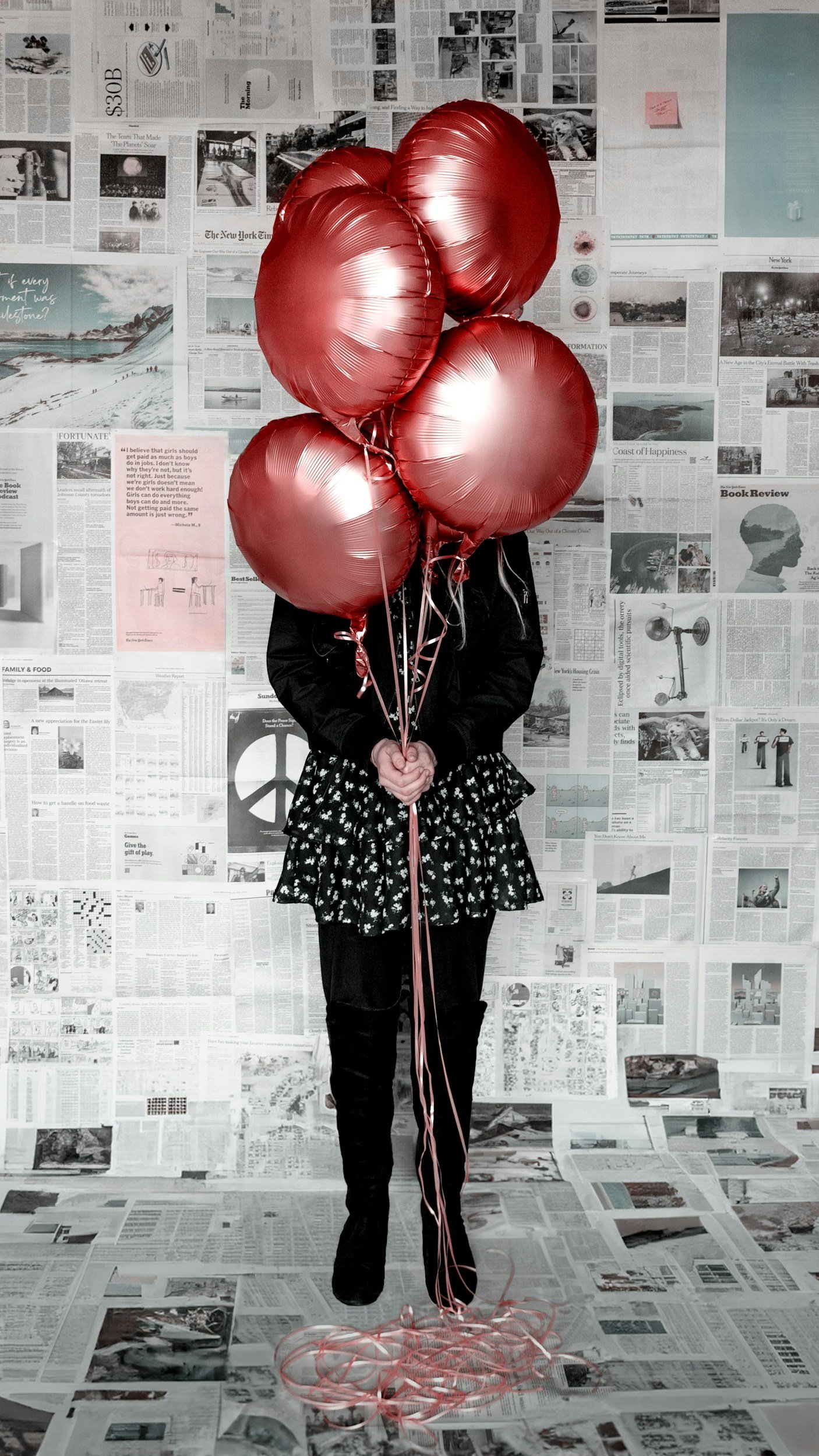 Person holding five red balloons in front of a wall covered with newspapers and magazines.