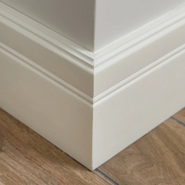 Close-up of a white baseboard molding at the corner of a room with wooden flooring.