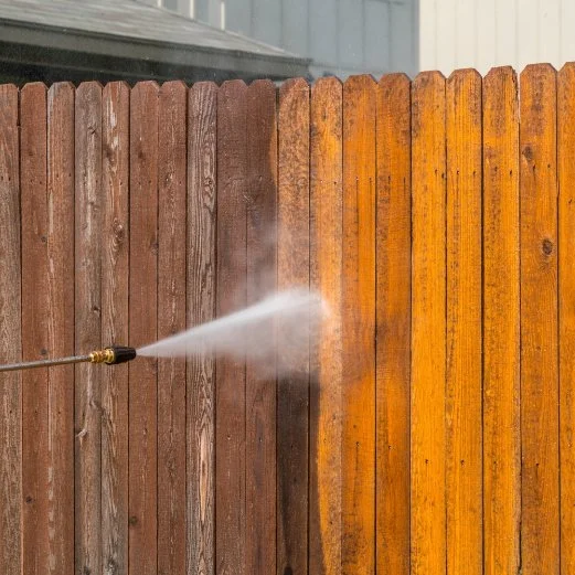 Power washer cleaning a wooden fence, removing dirt and grime.