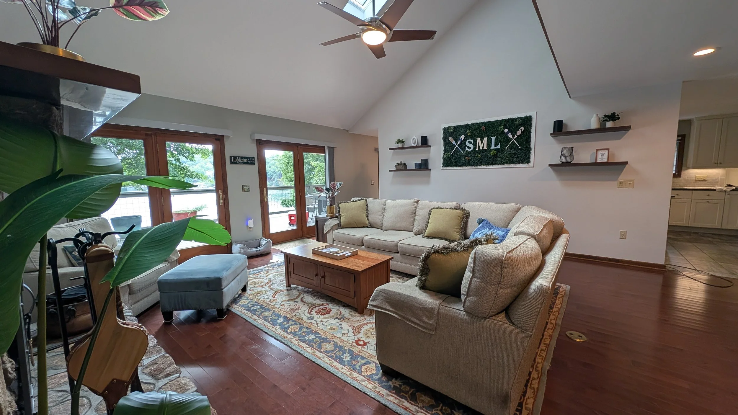 Living room with beige sofas, wooden coffee table, patterned rug, large glass doors leading outside, and ceiling fan. Smith Mountain Lake views from the living room and walk-out porch.