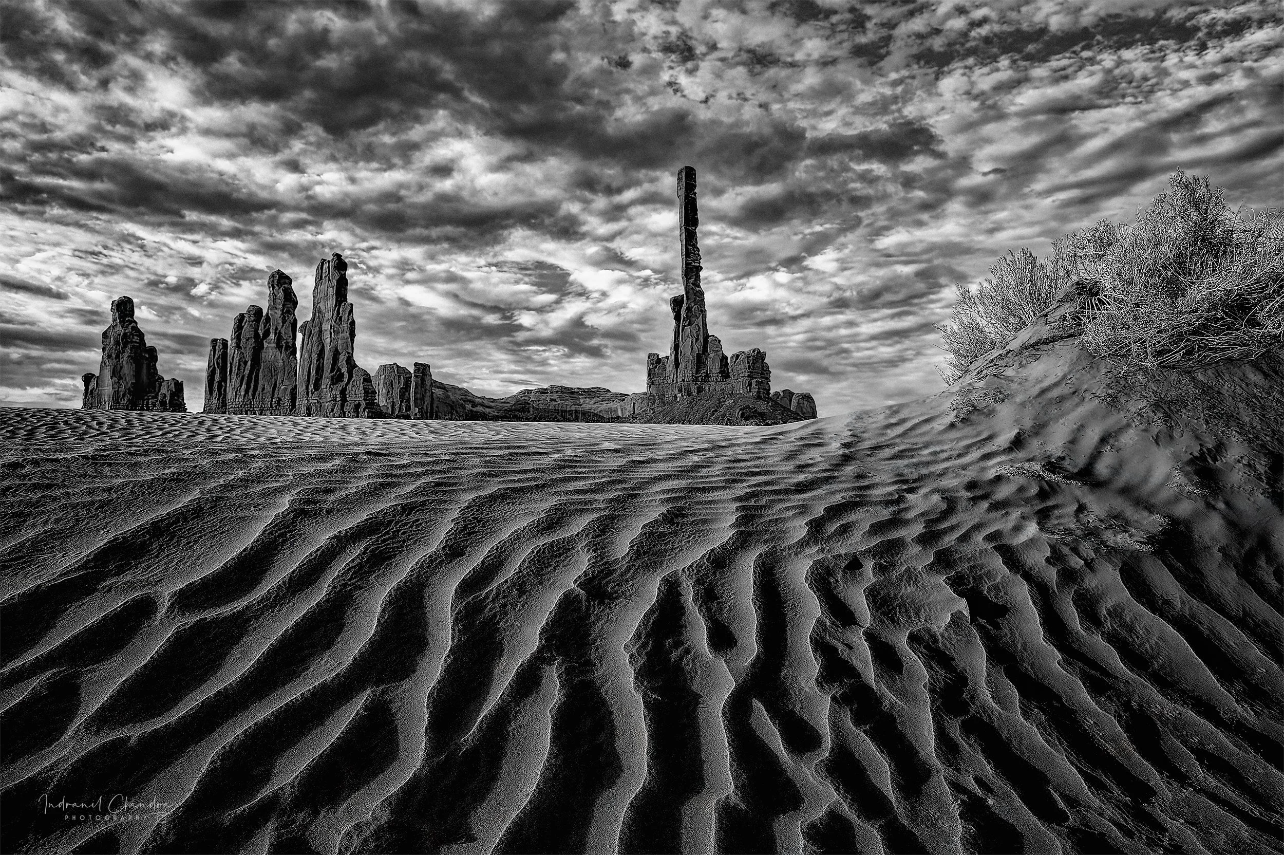 Wind-carved ripples in the sand lead the eye toward Totem Pole and the Yei Bi Chei formations, standing sentinel over Monument Valley in the early morning light. This stretch of dune sits within the Navajo Tribal Park, accessible only with a Navajo g