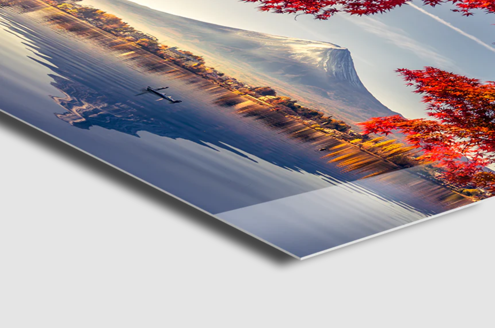 A serene landscape with a calm lake reflecting colorful autumn trees, a mountain in the background, and a boat on the water during sunset.