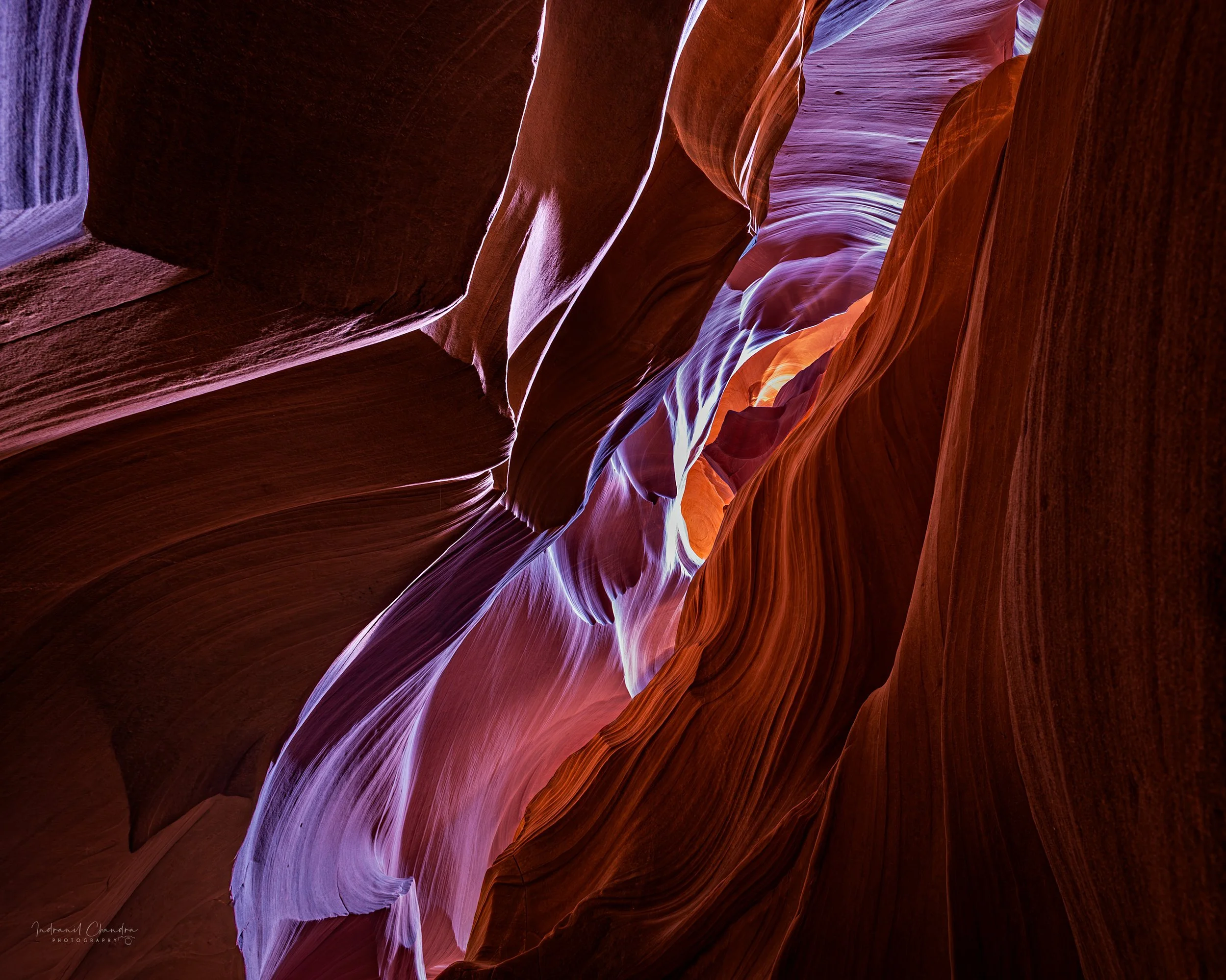 Curving sandstone walls catch and reflect desert light, shifting from deep umber to violet and ember-orange in this intimate abstract from Antelope Canyon.