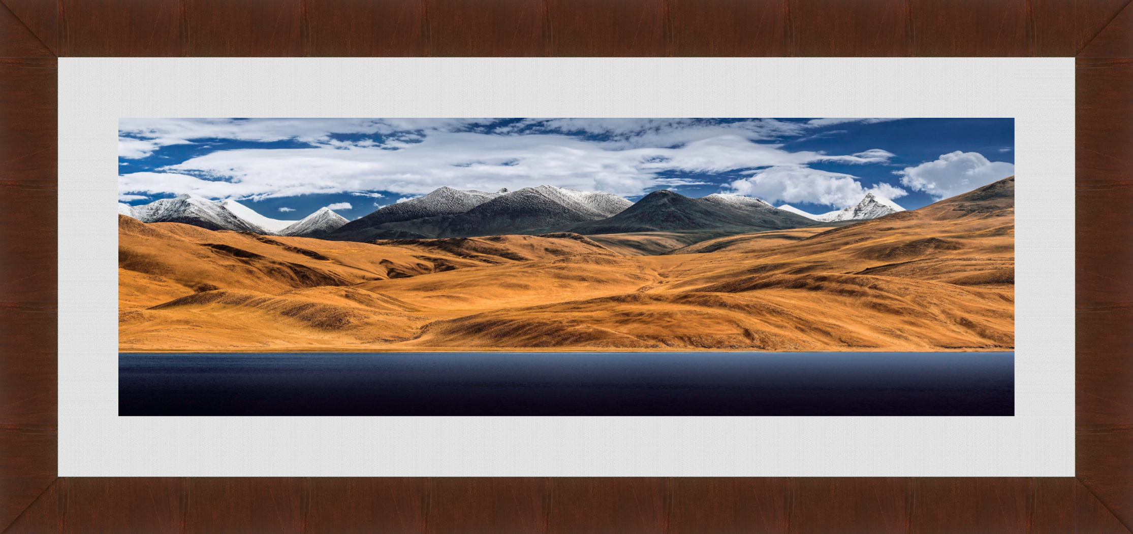 Landscape of rolling golden hills with snow-capped mountains in the background and a blue sky with white clouds.