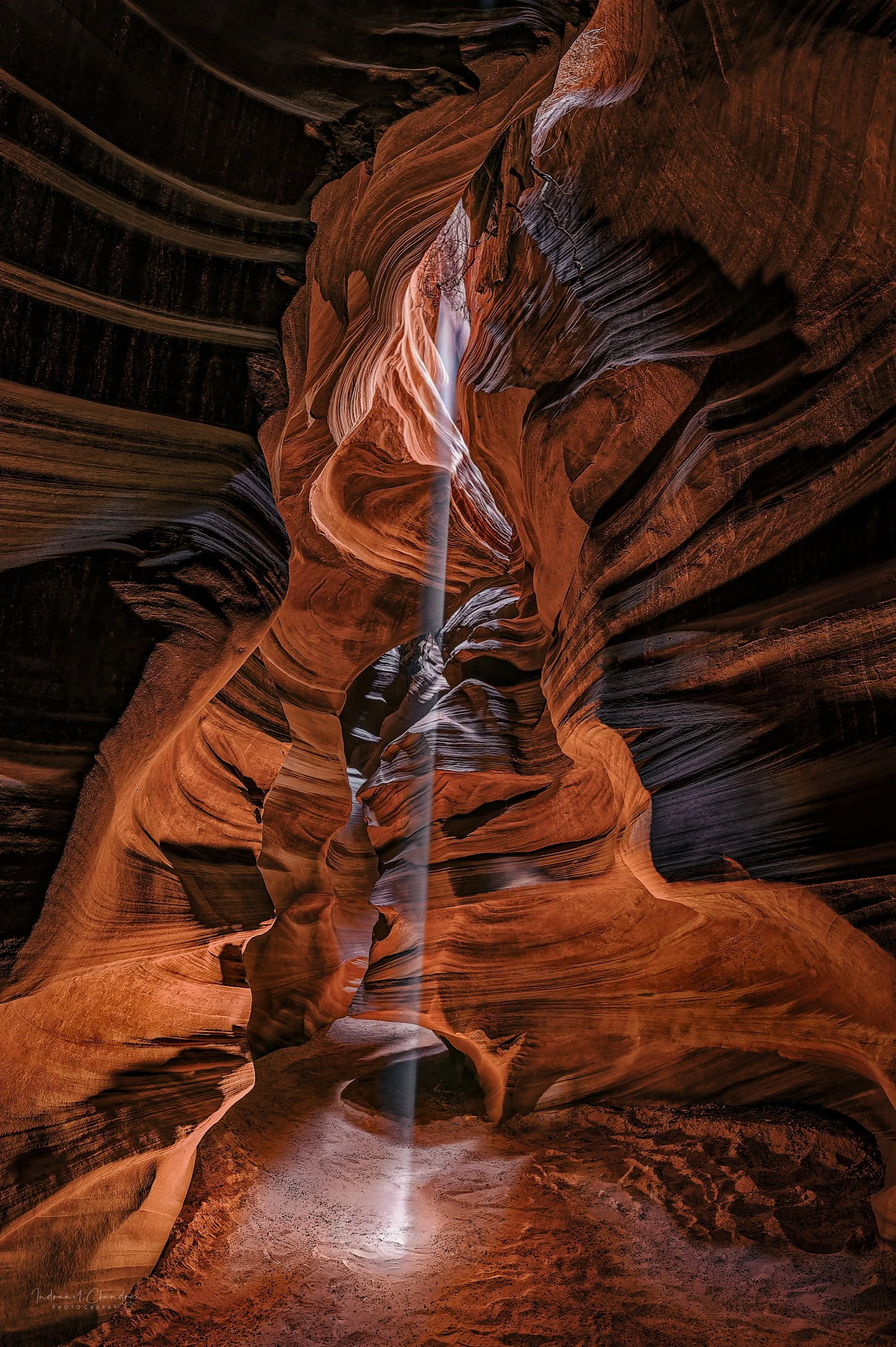 A beam of light, often called "God Beam", illuminates the wave-like sandstone walls in the Cathedral room of the Antelope Canyon, creating a contrast of light and shadow and highlighting the vibrant orange, red, and purple hues of the rock formations