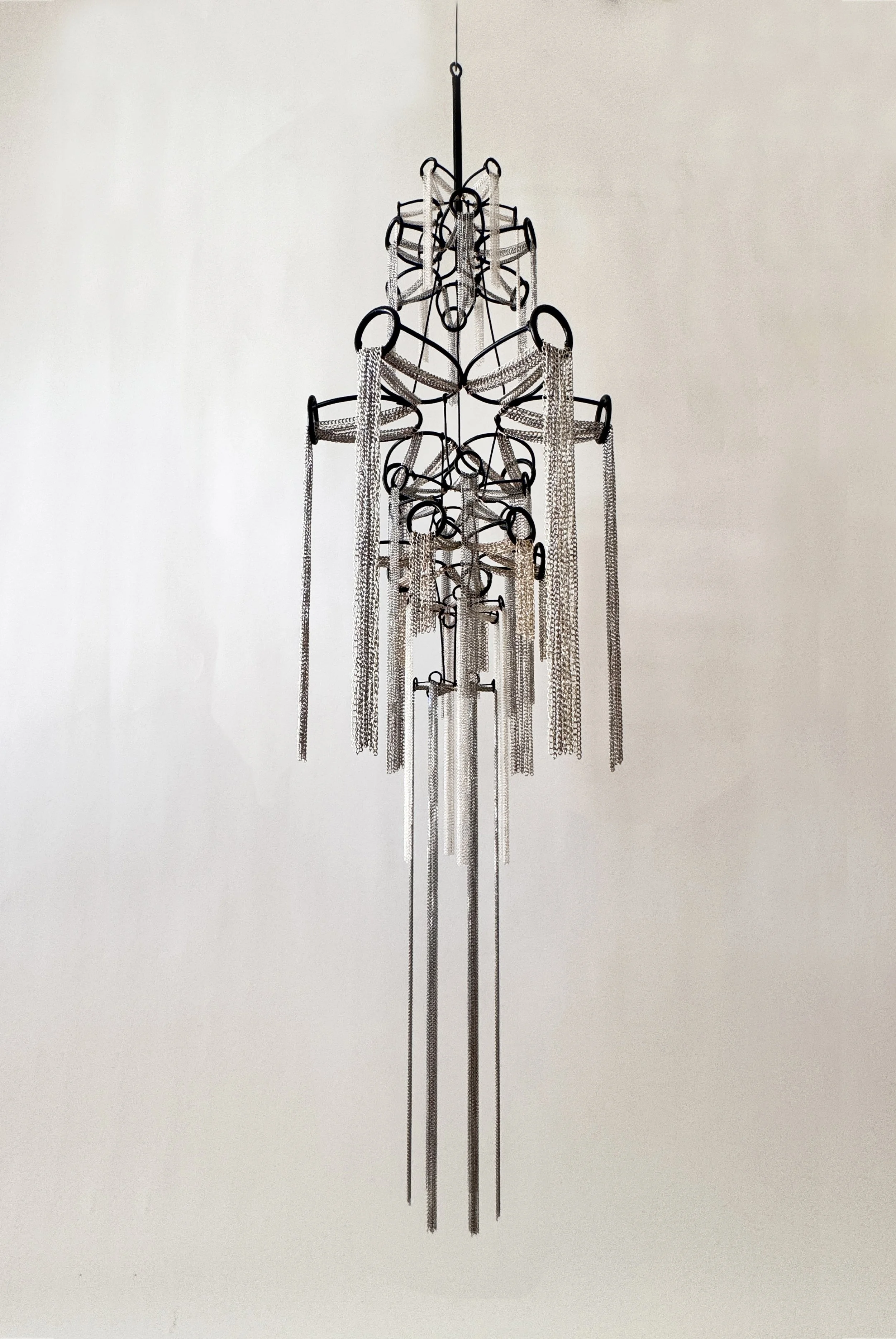 A suspended cascade of chains forms a feminine silhouette, inspired by women as the original water bearers—holders of milk, tears, blood, and emotion. Streams pour, honoring the life-giving waters women carry.