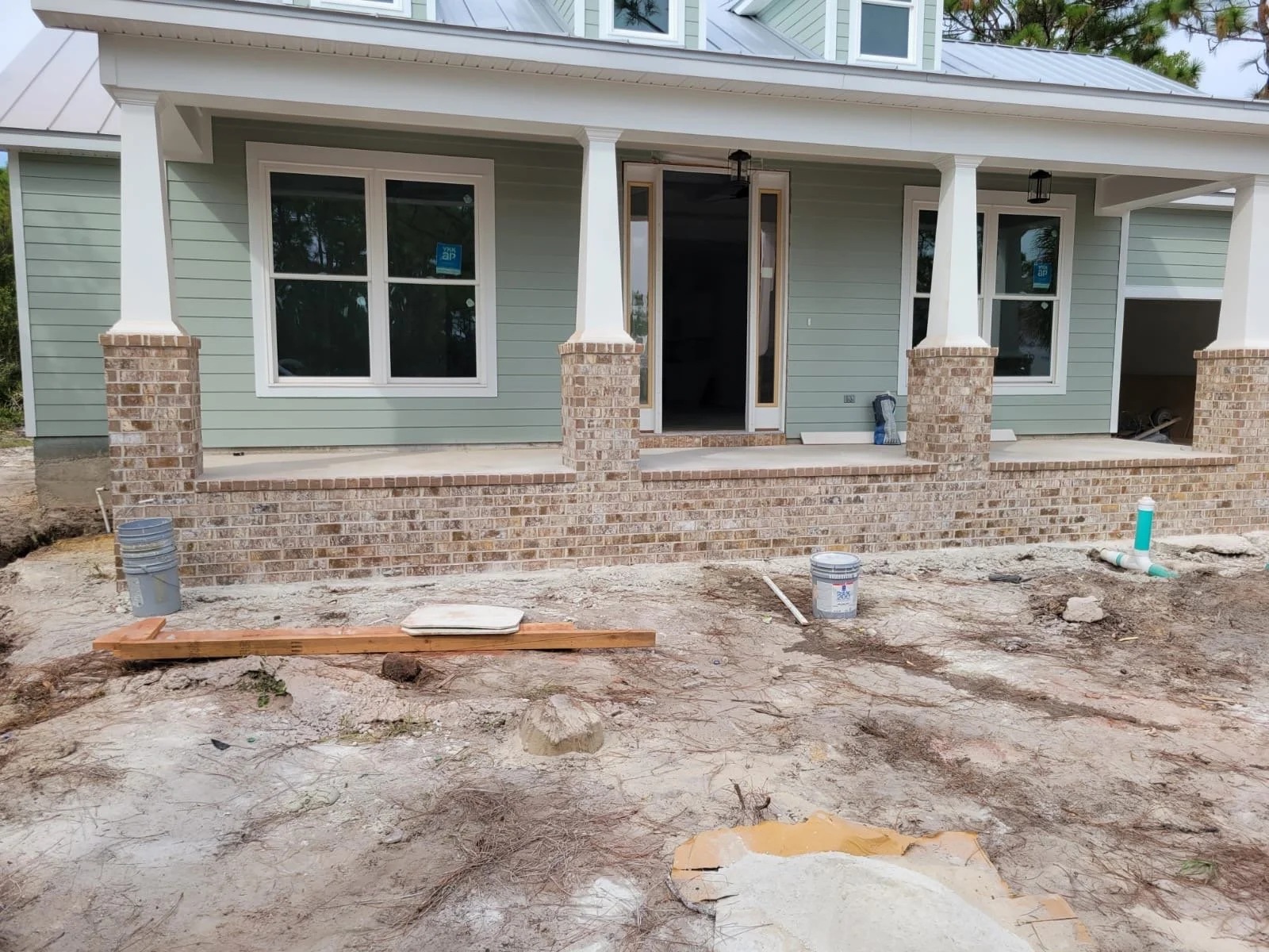 Construcción de una casa con jardín de ladrillos y muro de cemento, en proceso de acabado con materiales de construcción visibles en el suelo.