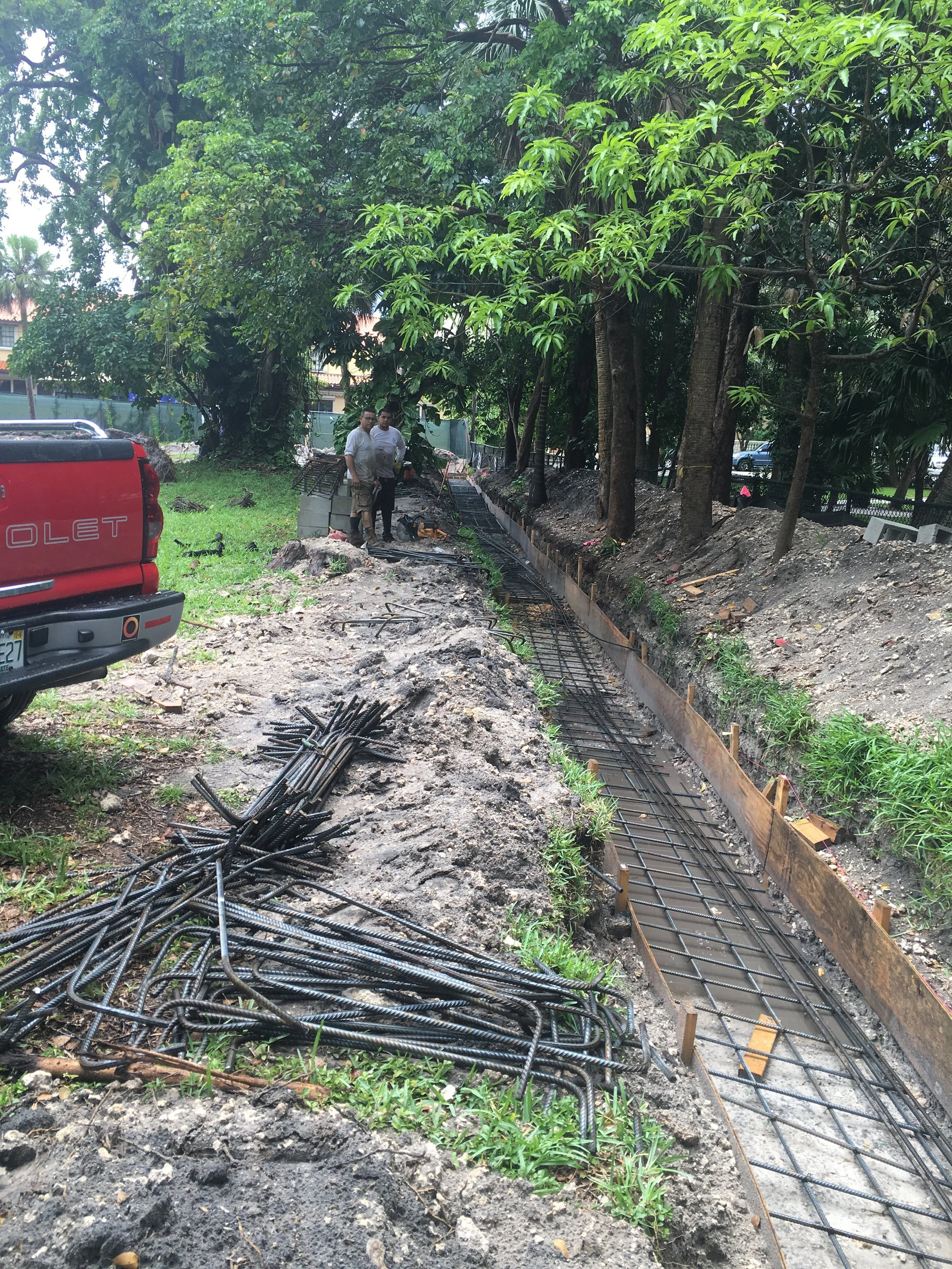 Trabajos en construcción de una vía de tren o ferrocarril en un espacio abierto con árboles, con algunos empleados en la zona.
