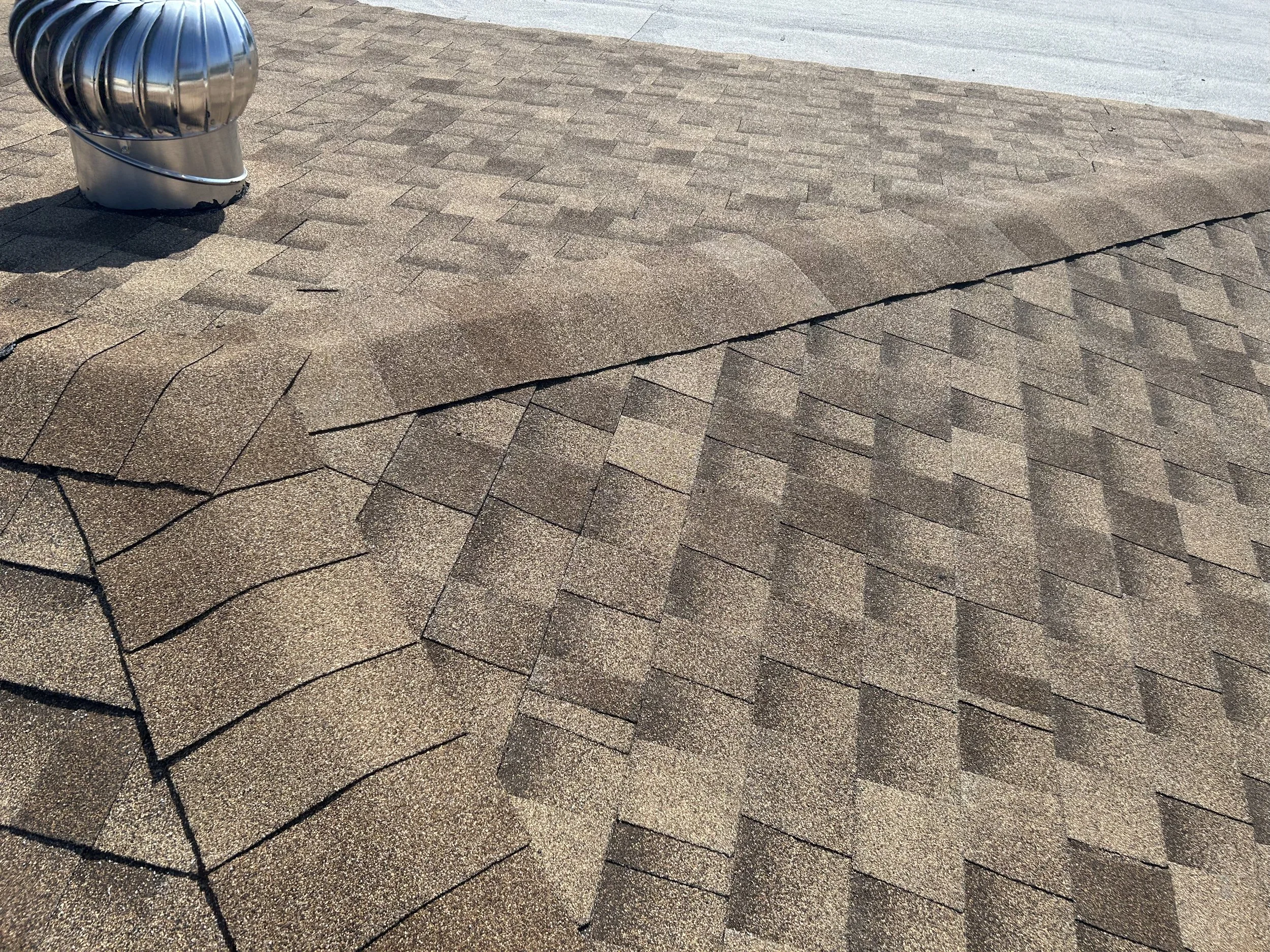 Tejado cubierto con tejas de asfalto en diferentes colores y un respiradero de metal en la esquina superior izquierda.