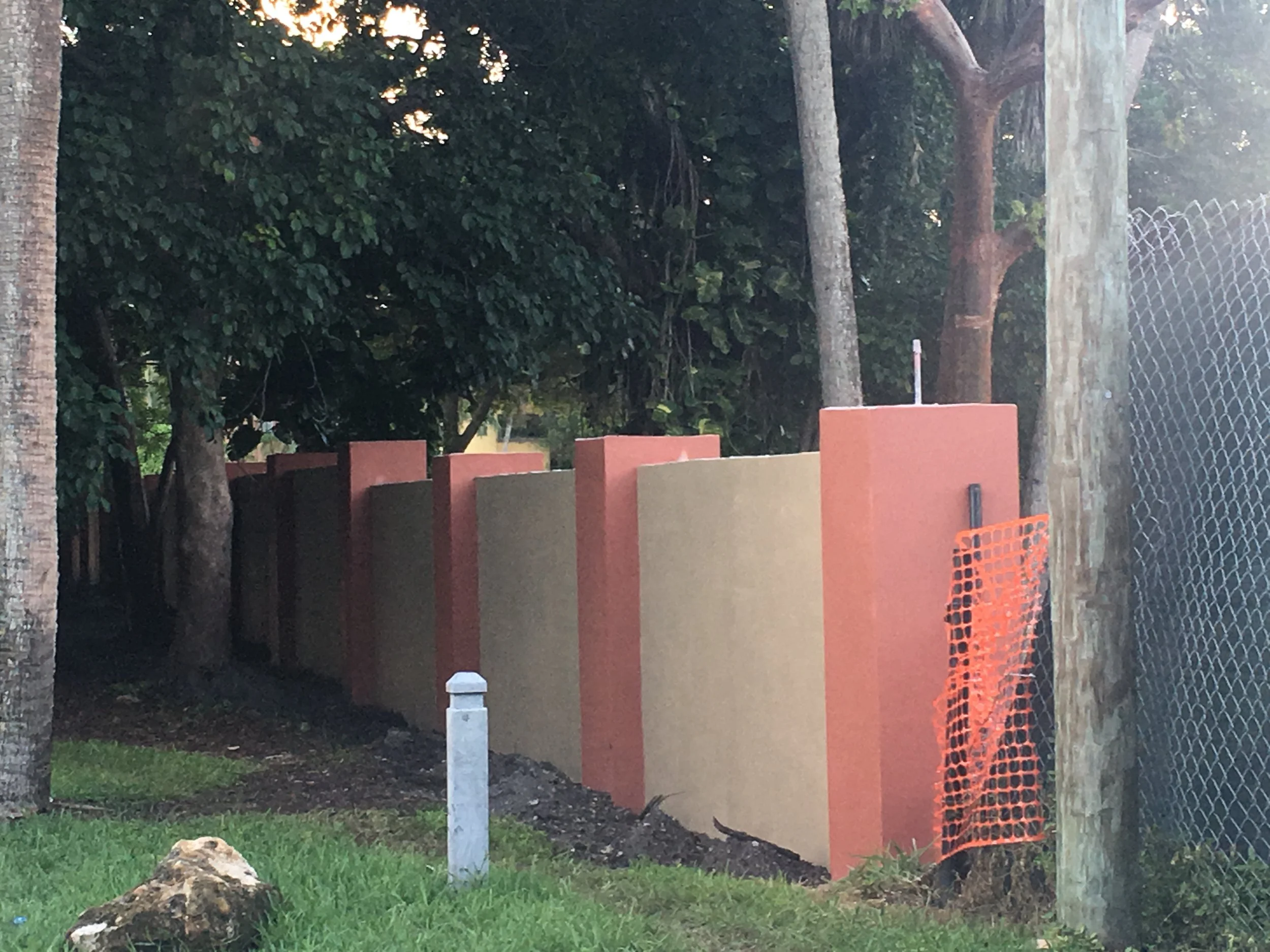 Muros de colores en construcción junto a árboles y cercas de malla en un entorno exterior.