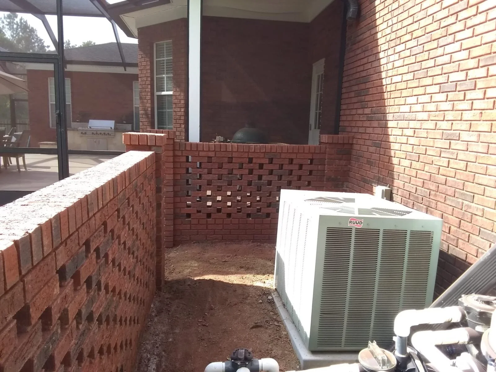 Espacio en un patio trasero con paredes de ladrillo rojo, una unidad de aire acondicionado y una estructura de pared de ladrillo en proceso de construcción.
