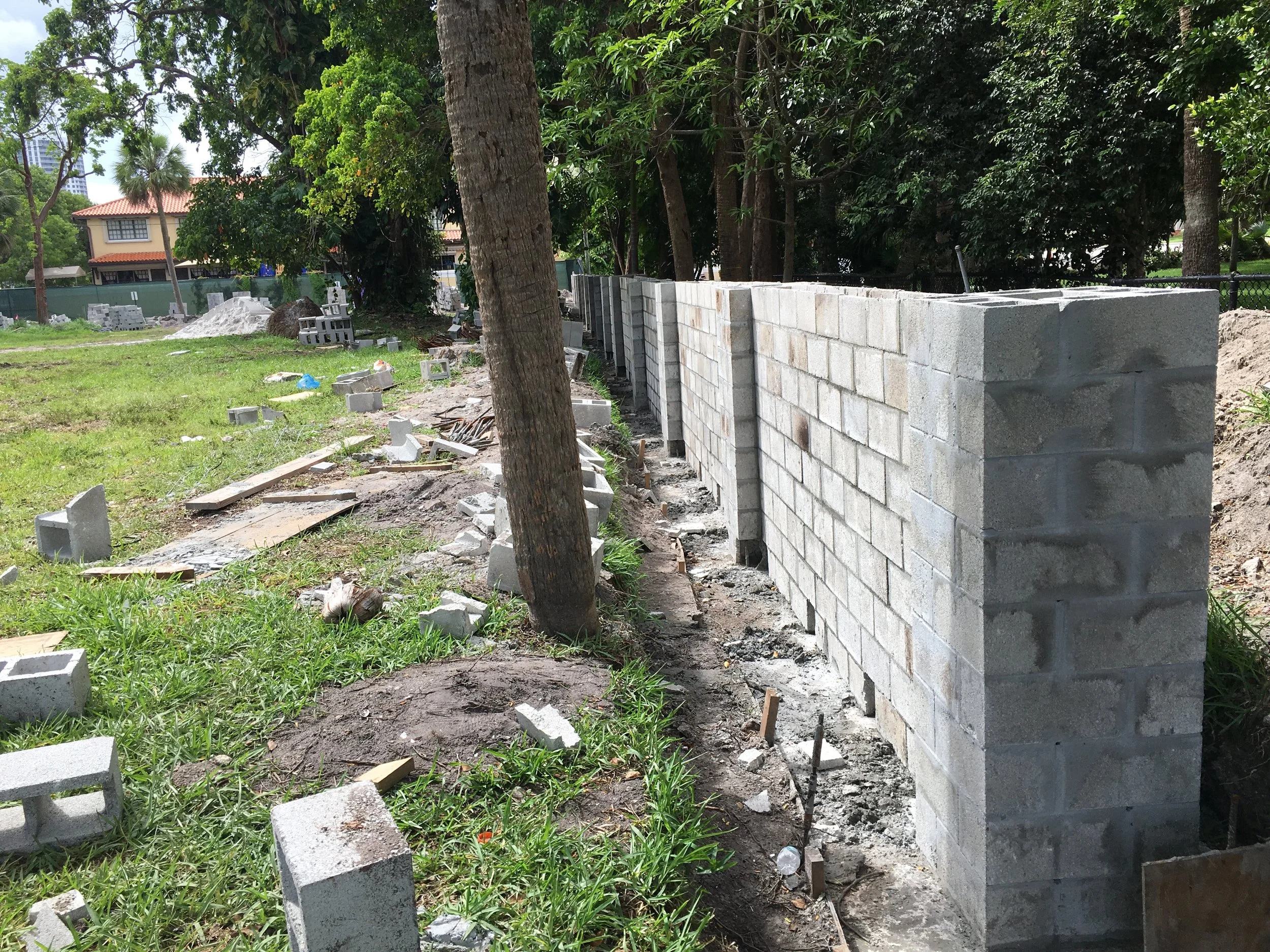 Construcción de un muro de bloques de cemento en un parque con árboles y césped, con materiales de construcción dispersos.