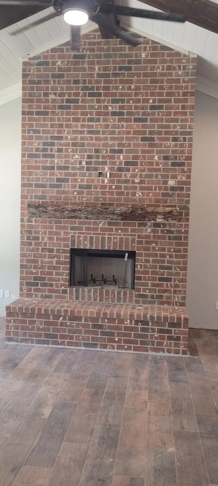 Muro de ladrillos rojos con chimenea empotrada y pared de madera en el techo, suelo de baldosas de color tierra.