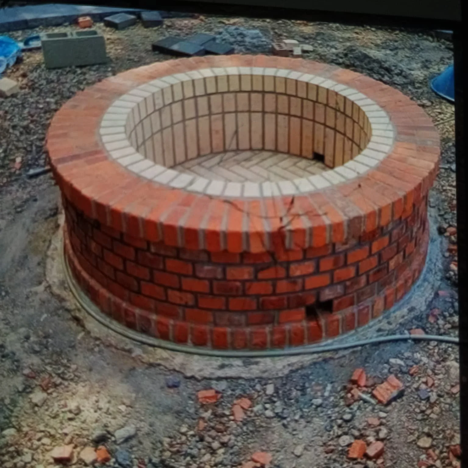 Estructura circular de ladrillos en construcción, con paredes internas y externas, en un sitio de trabajo.