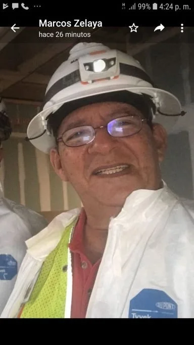 Hombre con casco y gafas, vistiendo una camisa blanca, en un entorno industrial o de construcción.