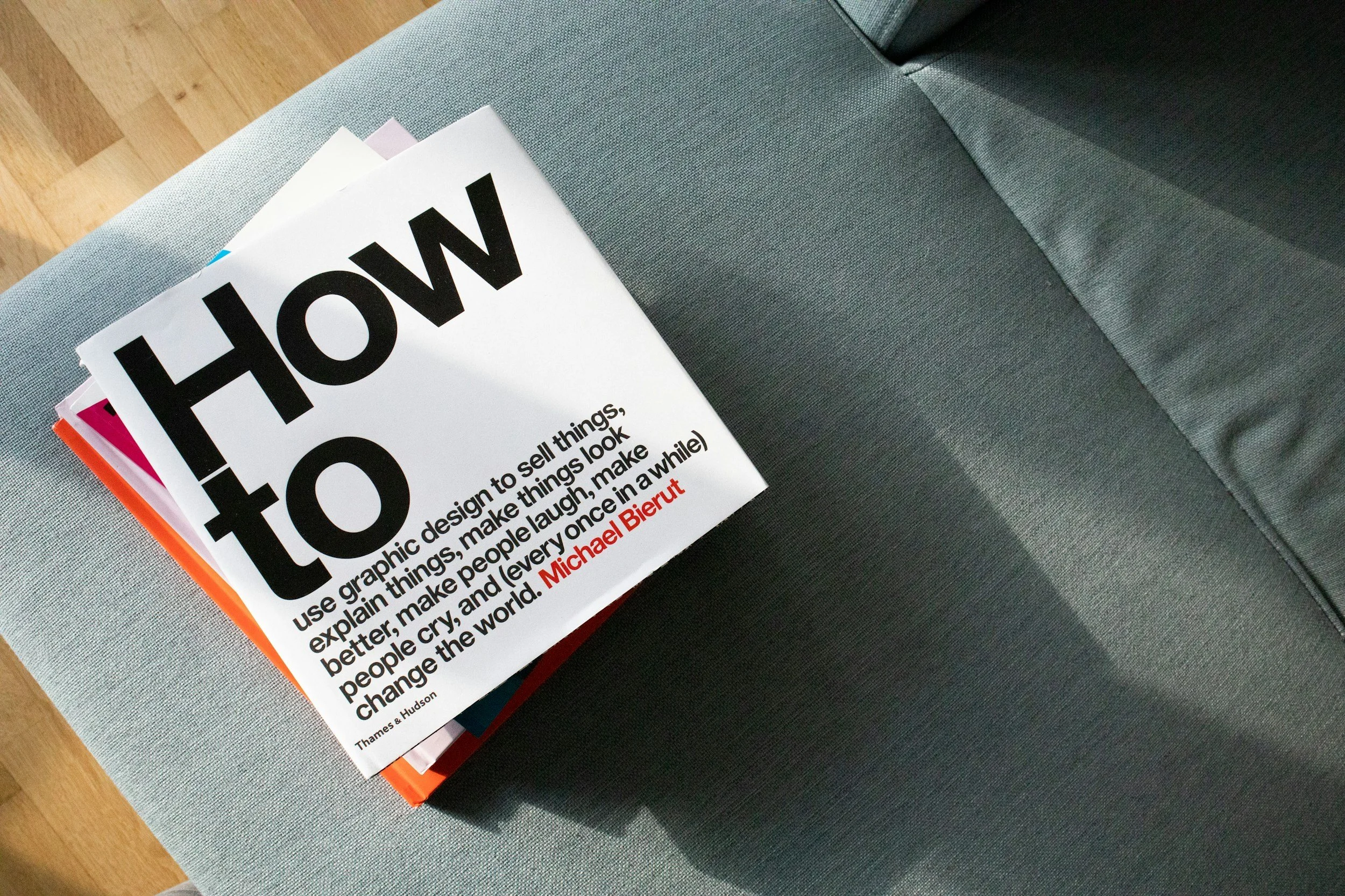 A booklet titled "HOW to" resting on a gray fabric couch, with a hardwood floor visible in the background.