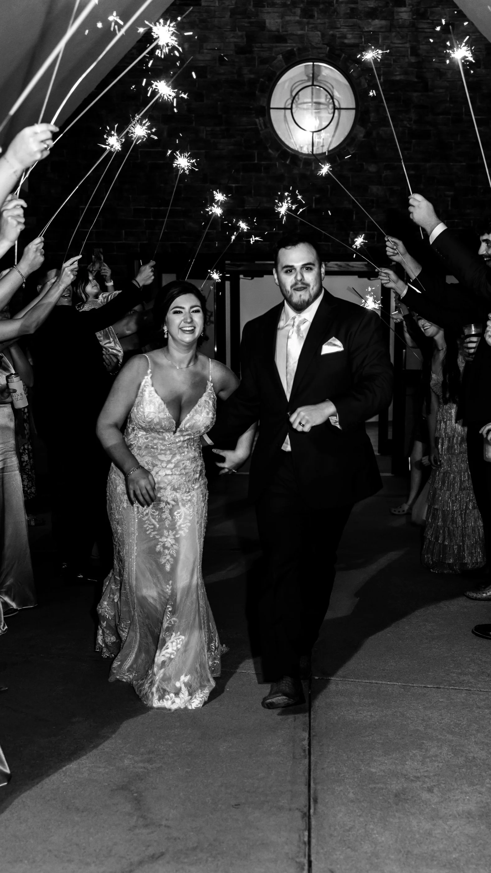 A newlywed couple walking hand in hand through a sparkler send-off at their wedding reception.