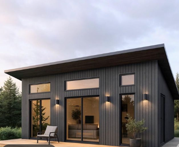 Modern black house with large glass windows and door, outdoor seating, and surrounding greenery under a cloudy sky.
