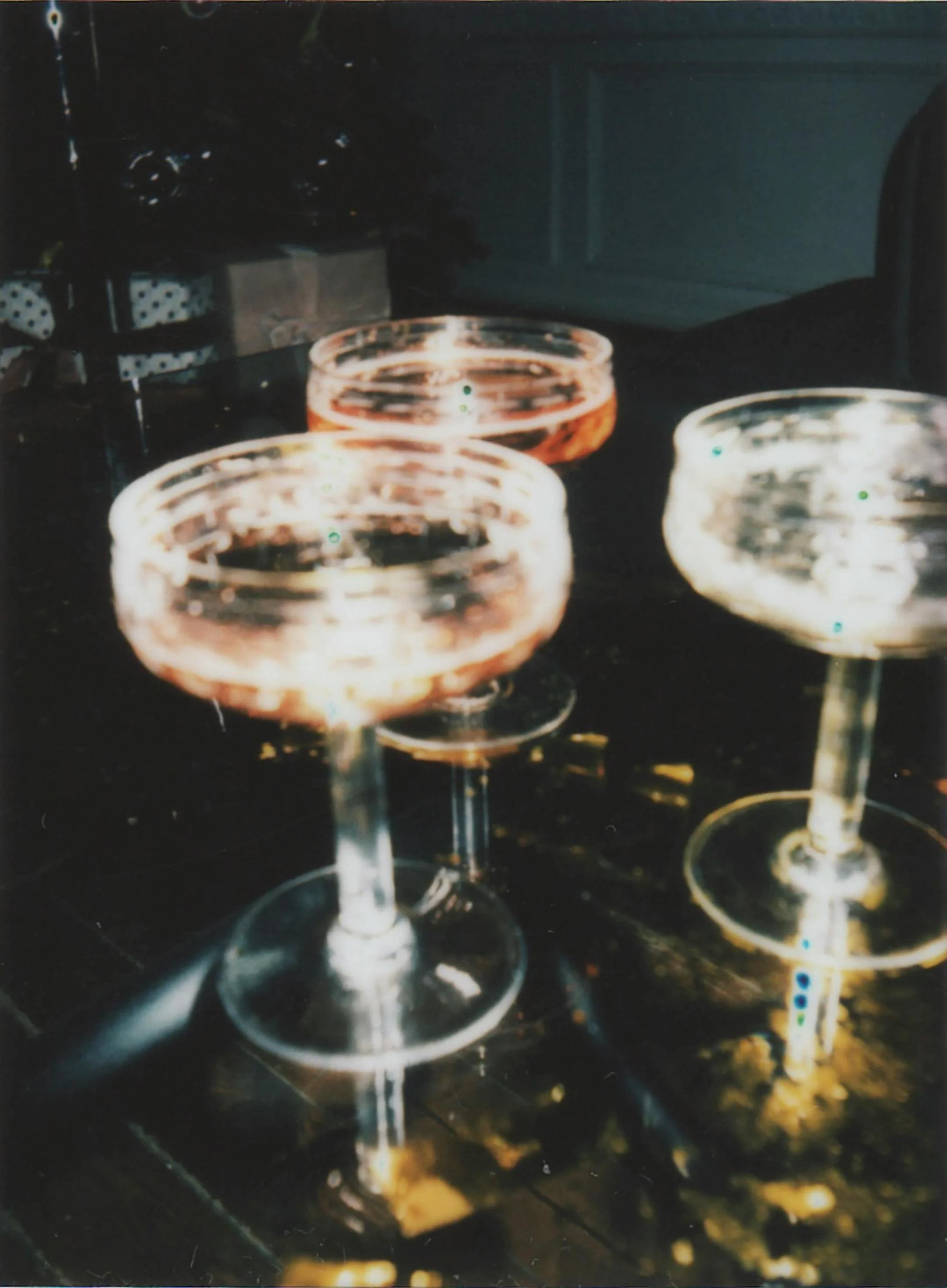 Three empty cocktail glasses with wide bowls and long stems on a dark surface, with a dimly lit background.