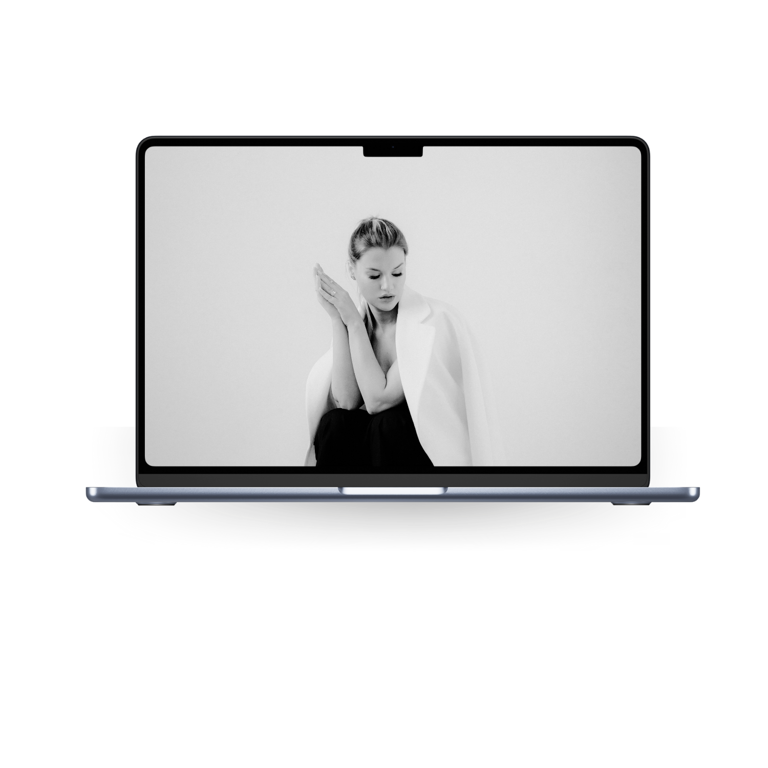 Black and white photo of a woman on a laptop screen, dressed in a white blazer, with her hair in a bun, posing against a plain background.