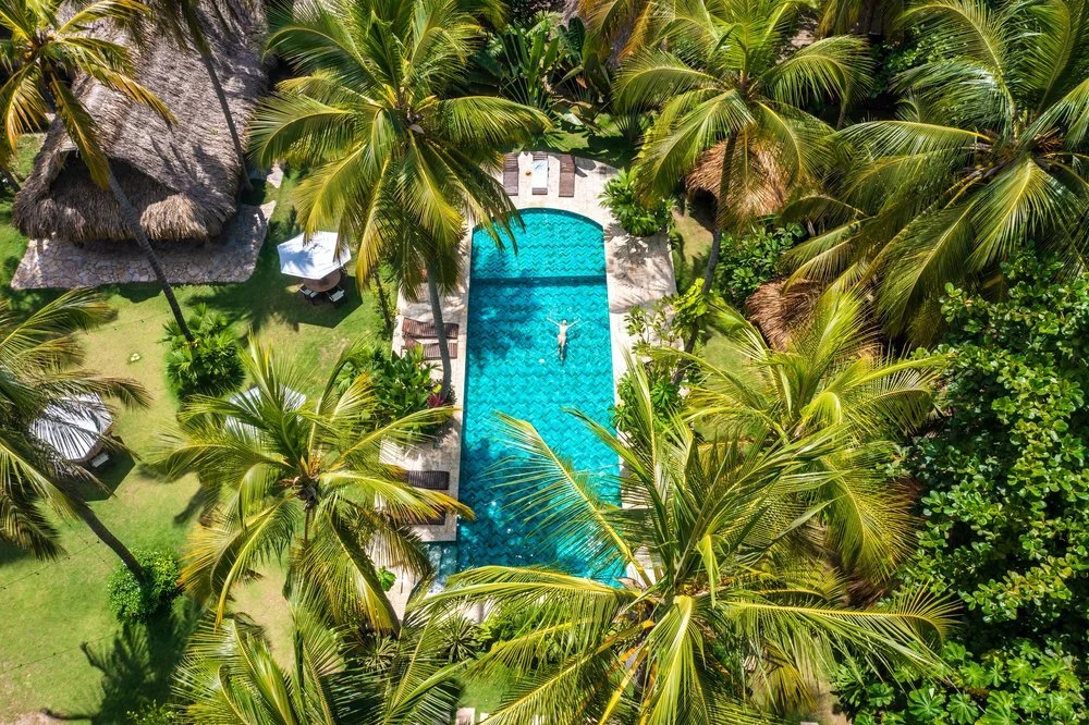 A person relaxing in a swimming pool surrounded by lush tropical palm trees and greenery at a resort.