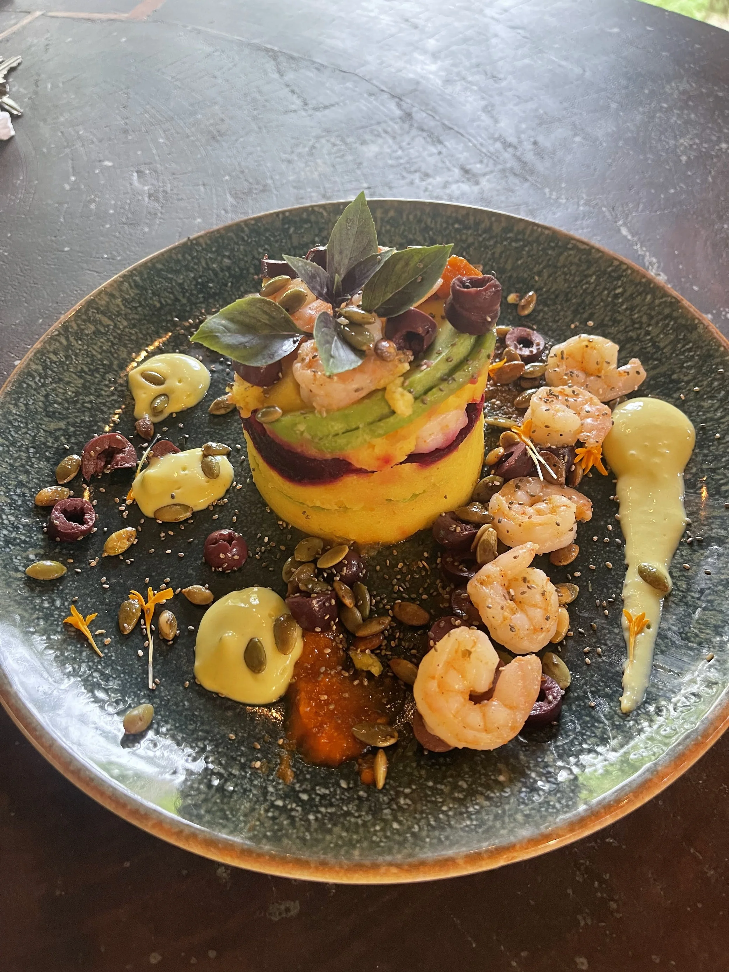 Elegant dish with shrimp, avocado, and garnish on a decorative black plate.