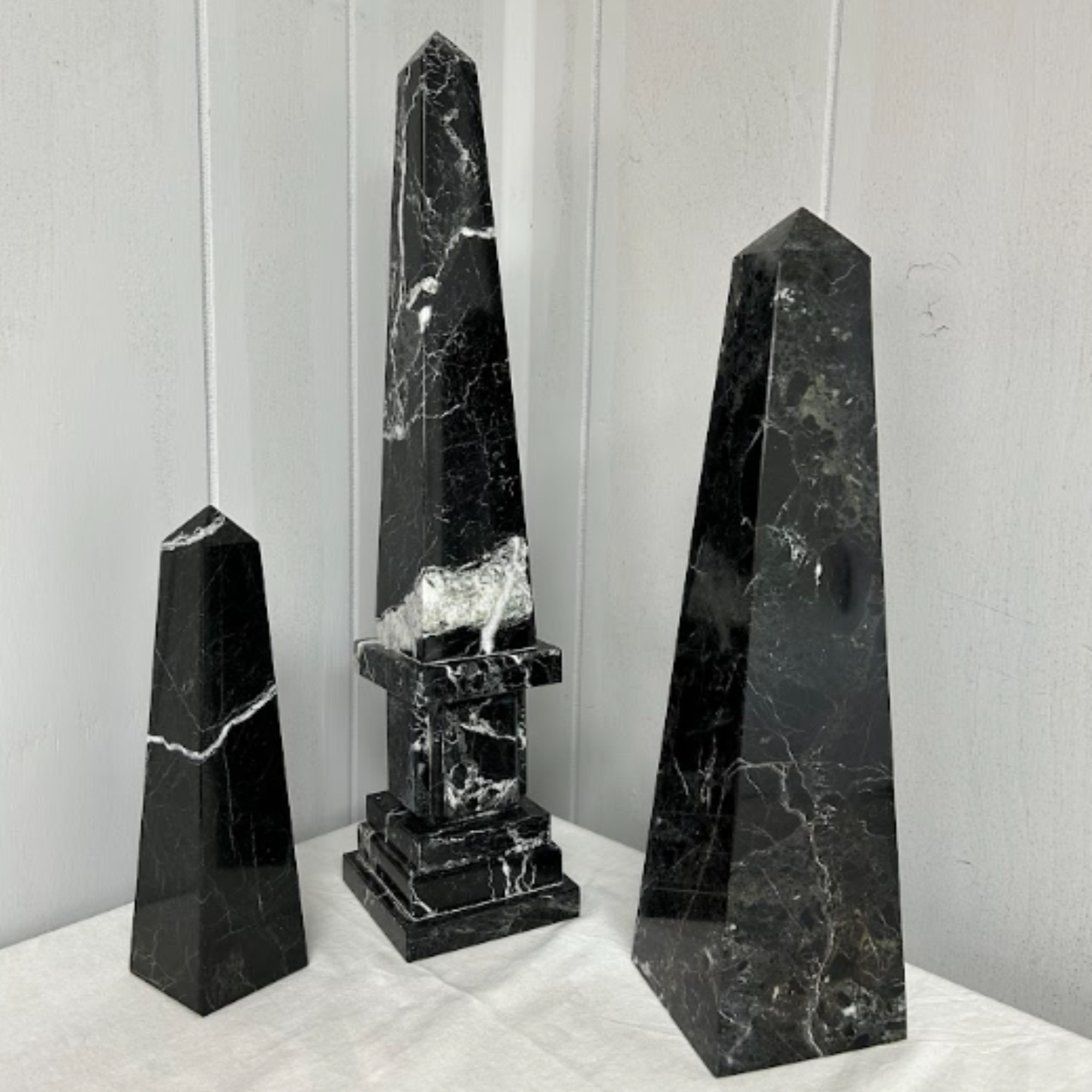 A black marble fountain with three vertical spouts of water, set against a white wall with paneling.