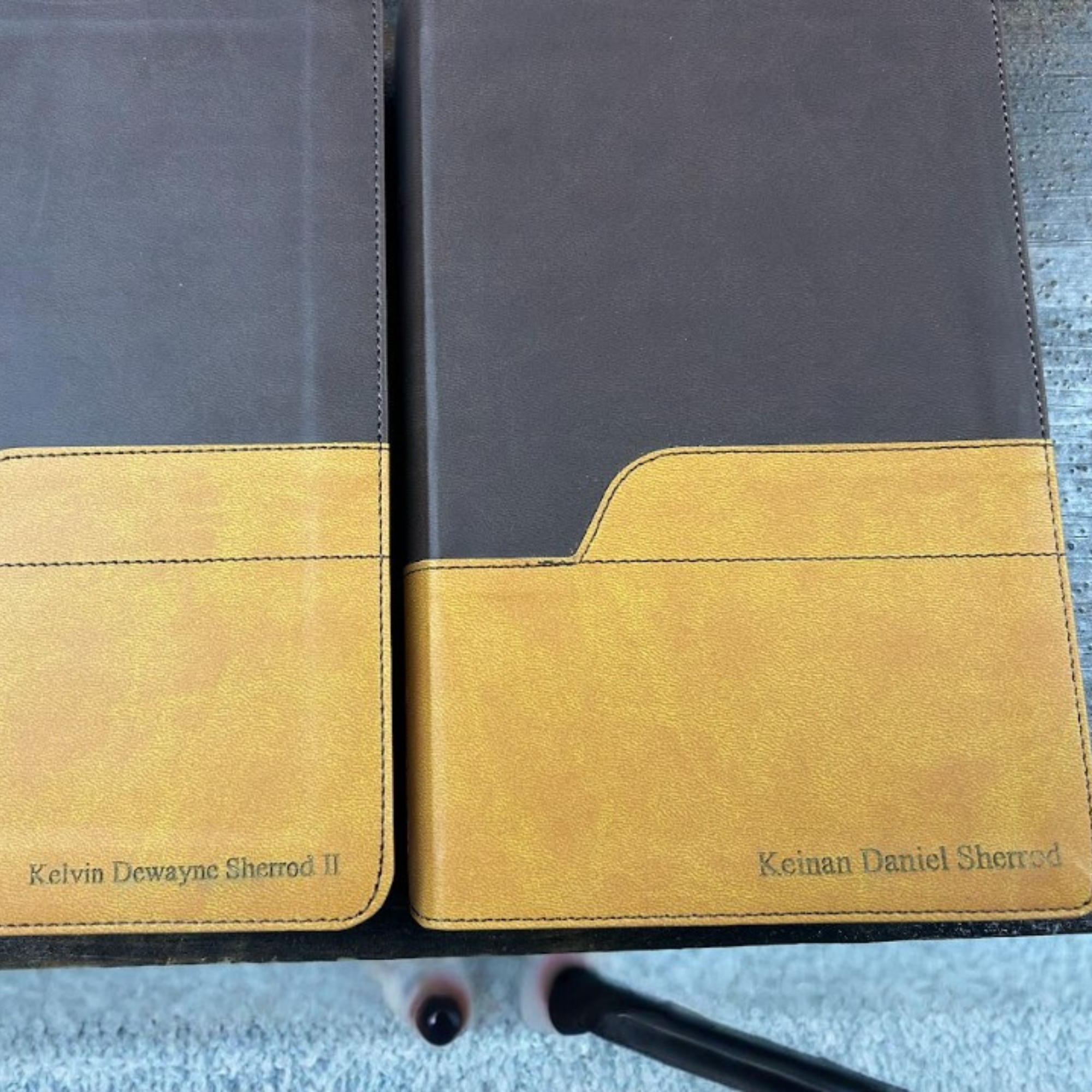 Close-up of two library books with yellow and black covers, placed side by side on a surface. The titles of the books are partially visible, featuring the names Kelvin Dewayne Sherrod II and Keinan Daniel Sherrod. The photo is taken from above, inclu