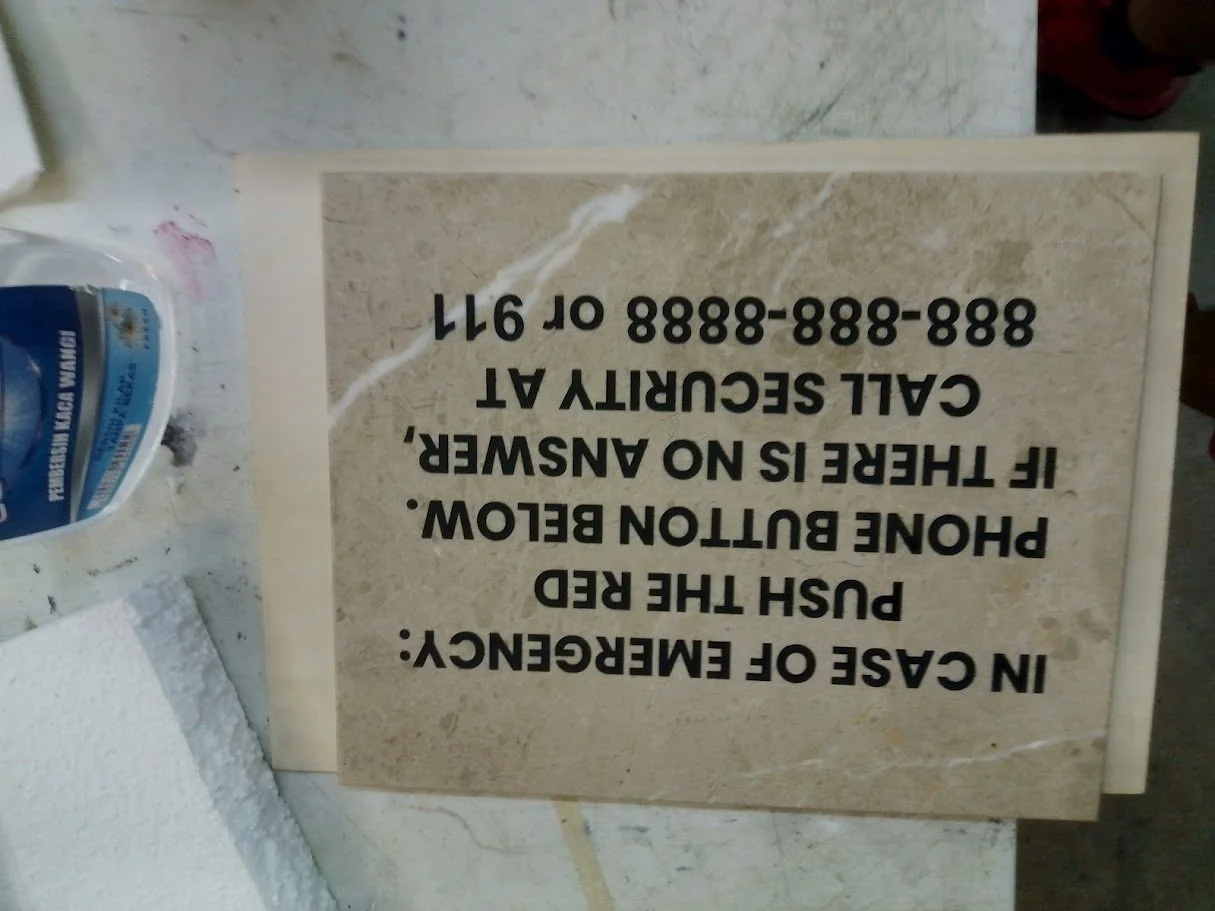 Sign with phone number and instructions in large black text on a beige marble background, laying on a work surface. The image is upside down.