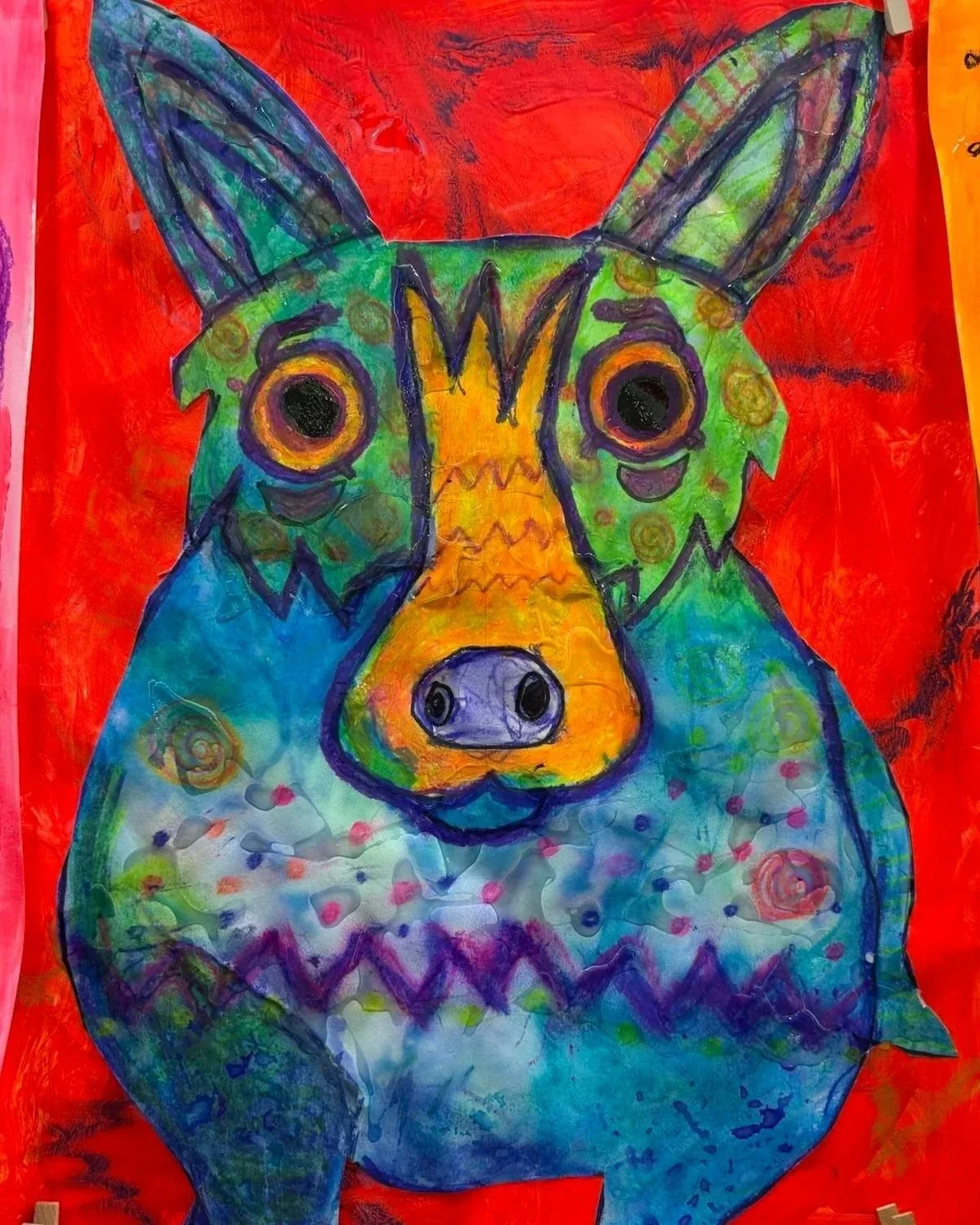 Colorful drawing of a creature with a rabbit-like face combining a pig's snout, large round eyes, and ears. Bright colors include green, yellow, blue, and purple on a red background.