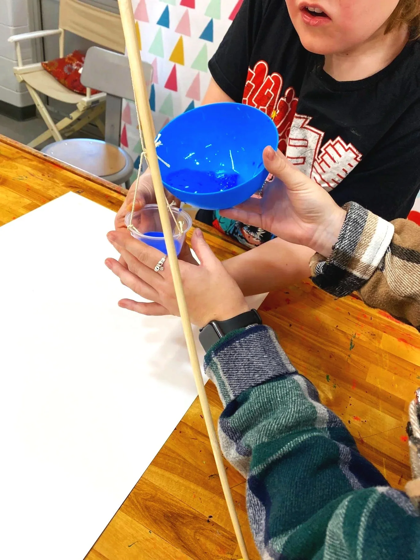People holding a small plastic container and a blue bowl during a craft activity at a wooden table.