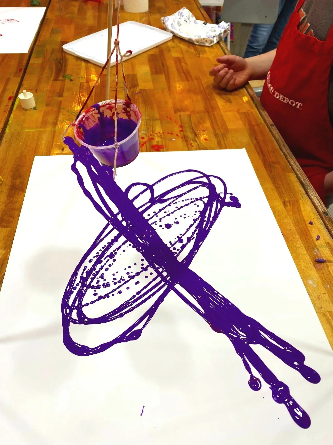 A painting of a spatula and a wine glass, created with purple liquid on a white paper surface.