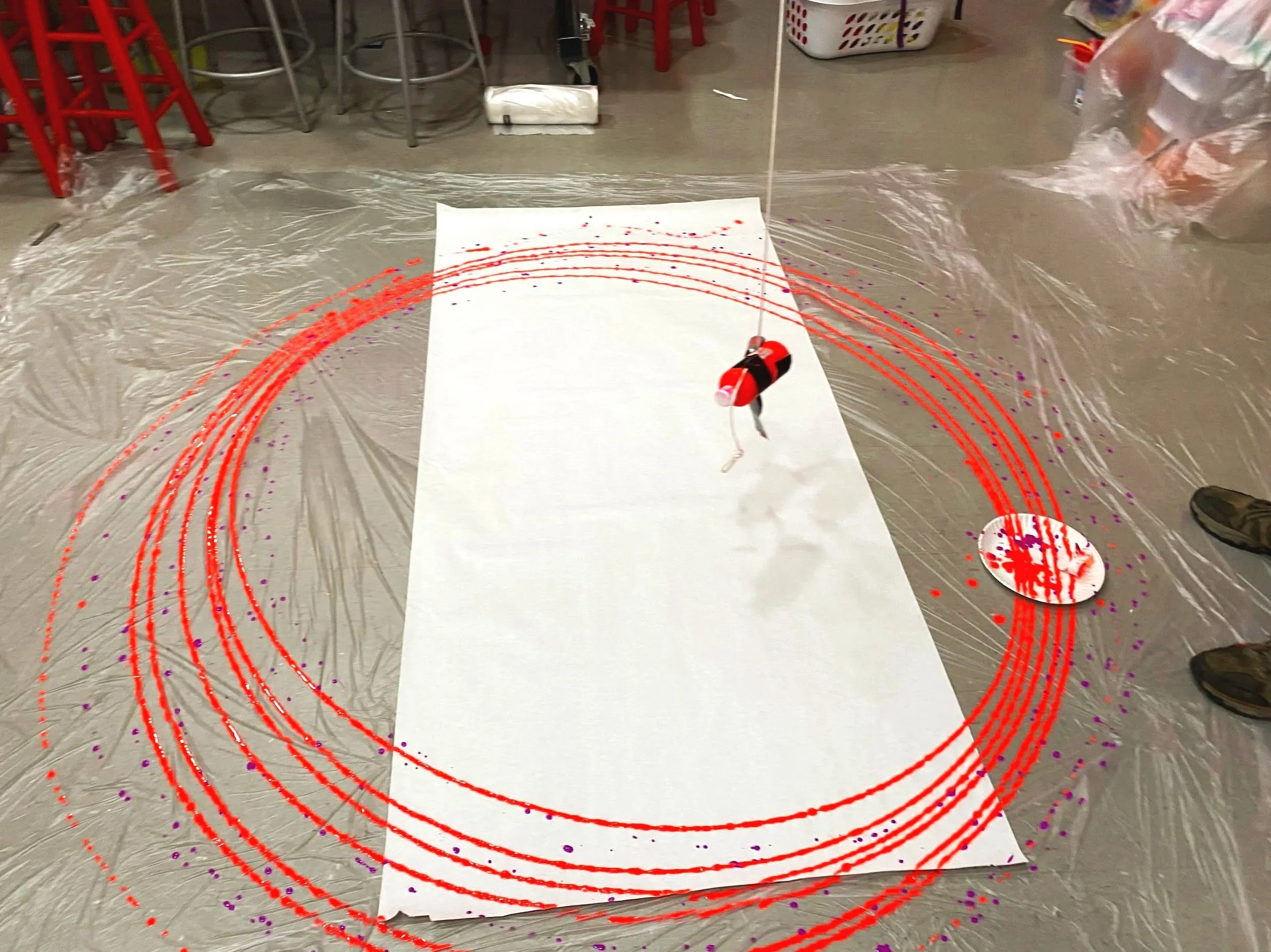 Adapted art classroom creating pendulum artwork showing movement in art. Laboratory setup with a white sheet of paper, a balloon, and digital overlay of red orbit-like circles and purple dots. 