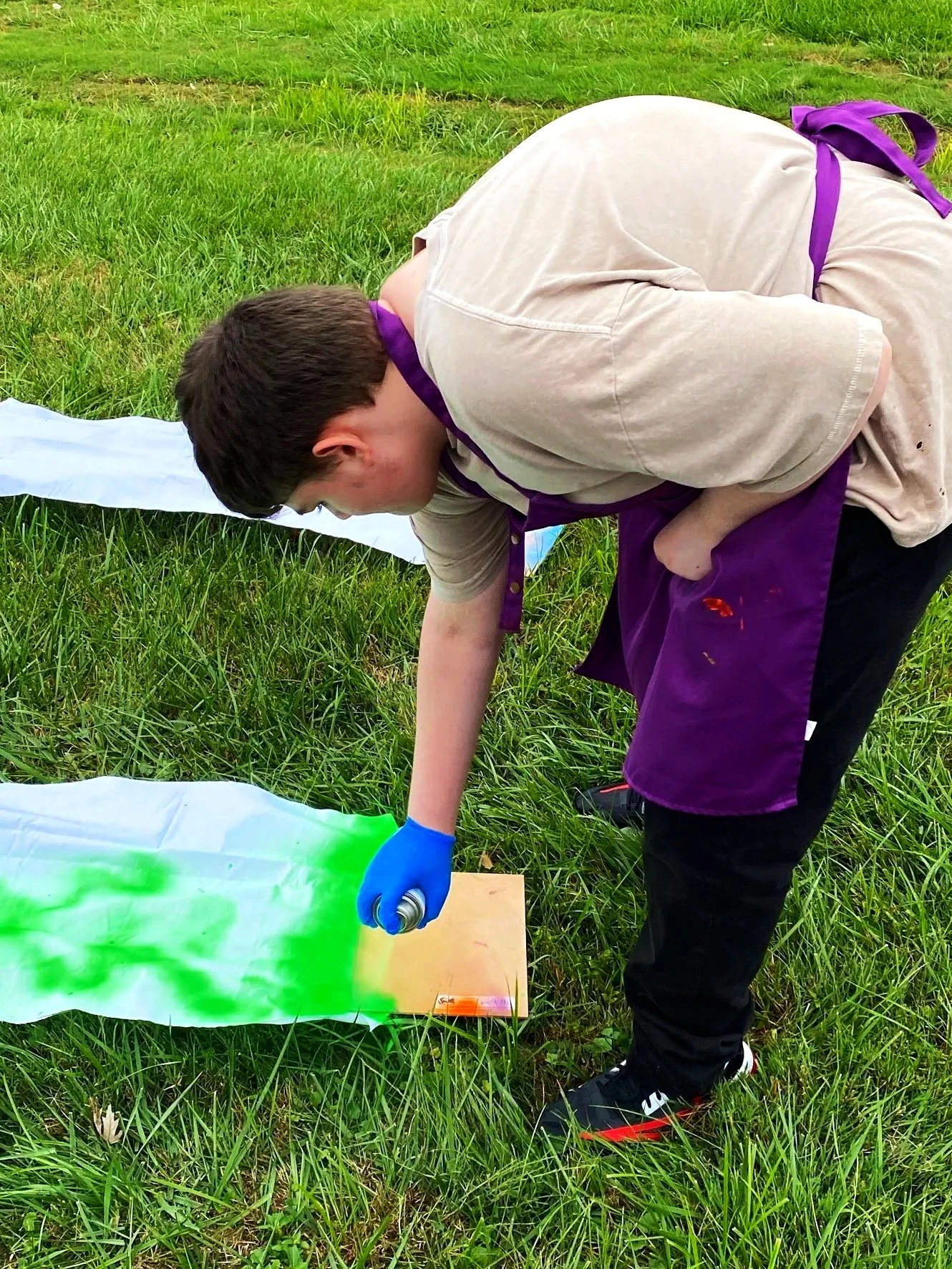 Person in beige T-shirt and black pants spray painting fabric outdoors