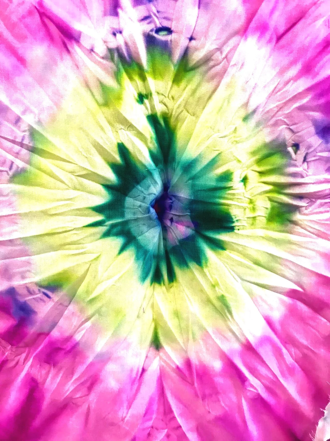 Close-up of a colorful, crumpled paper with a central tie-dye pattern in pink, yellow, green, and purple.