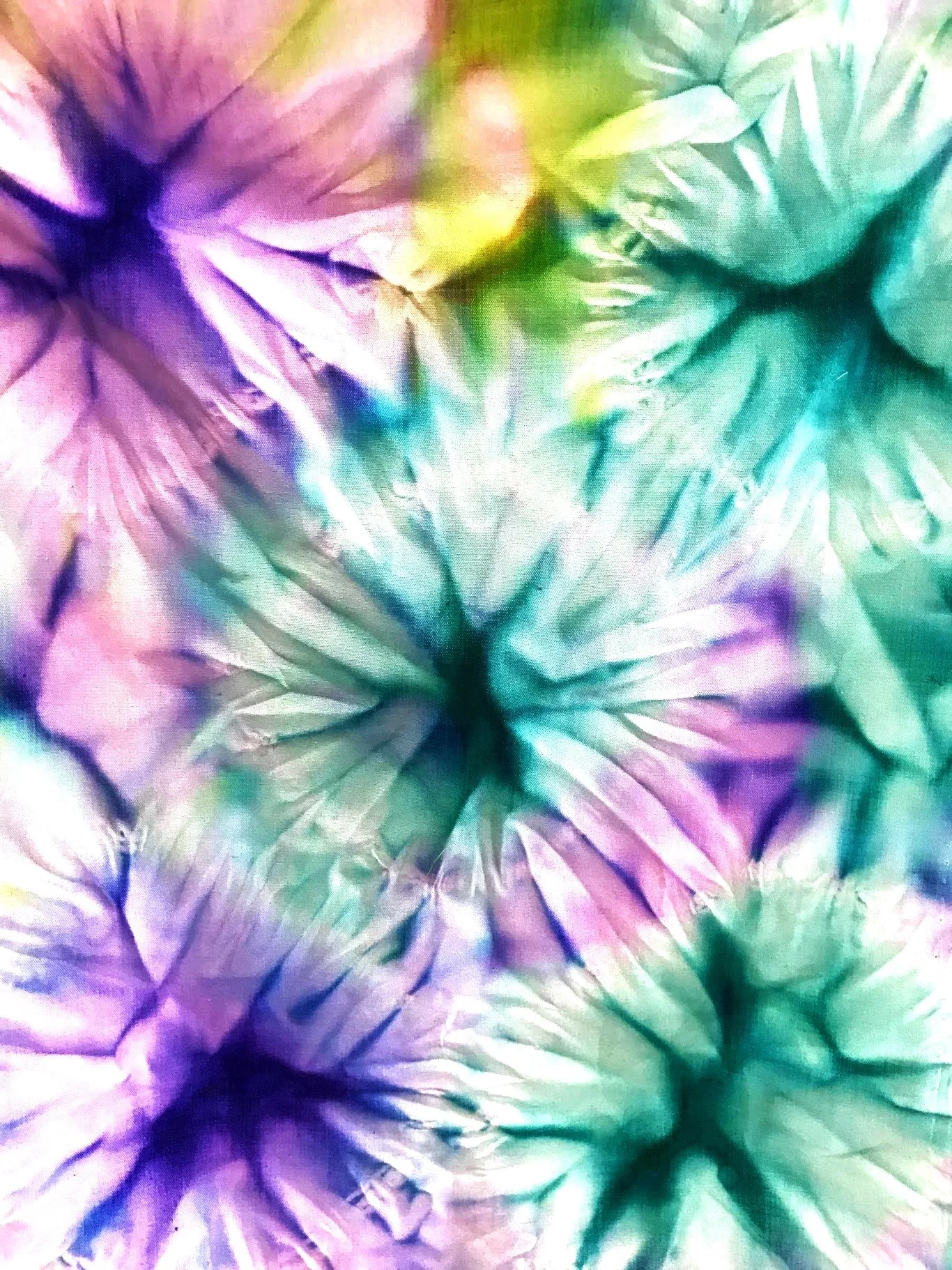 Close-up of a colorful tie-dye fabric with shades of purple, pink, blue, green, and yellow creating a spiral pattern.