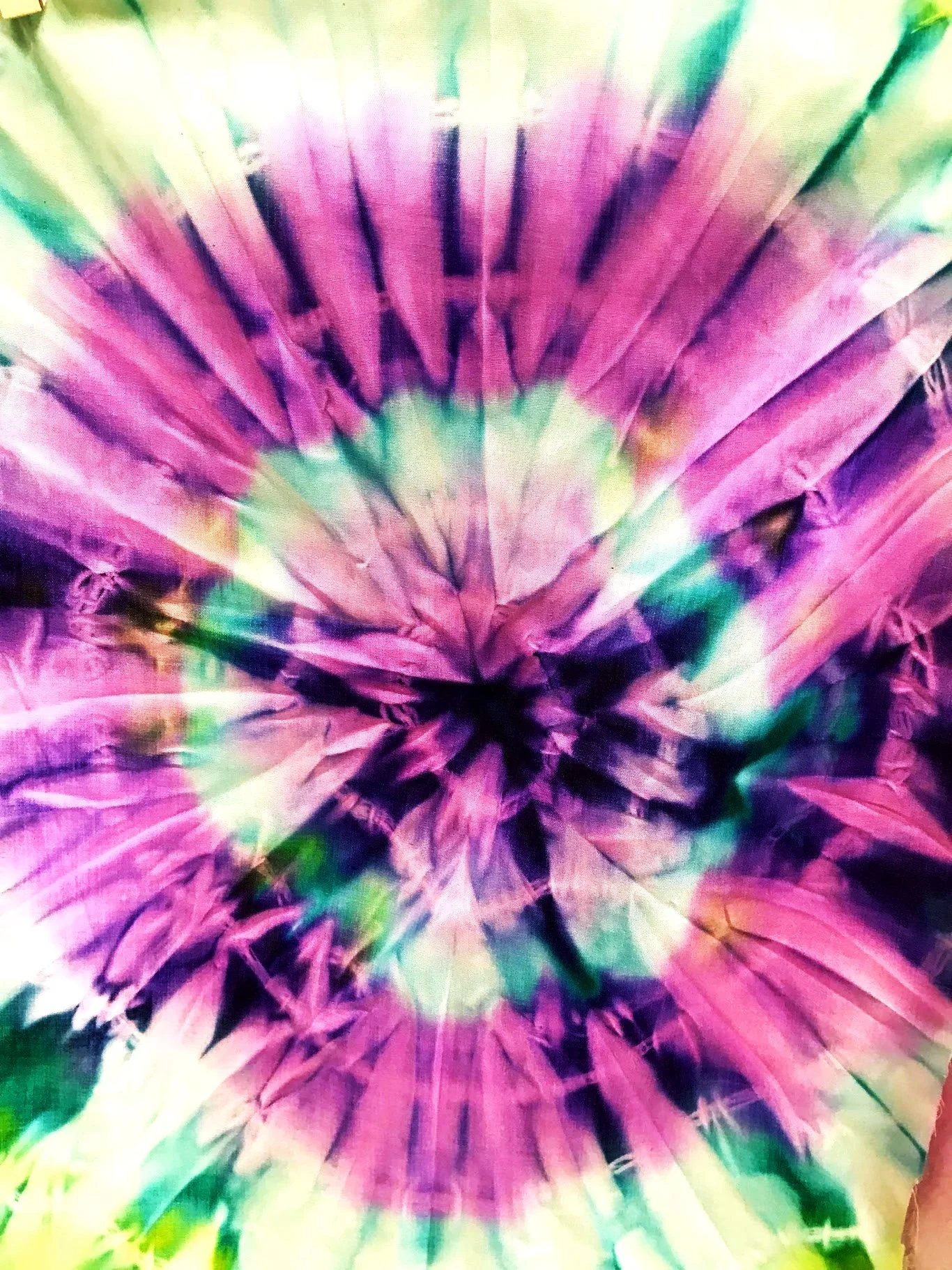 Colorful tie-dye fabric with pink, purple, green, and yellow hues forming a circular pattern.