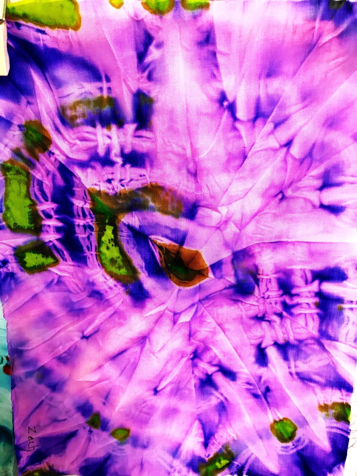 Close-up of a tie-dye fabric with purple, pink, blue, green, and brown colors in swirling and irregular patterns.