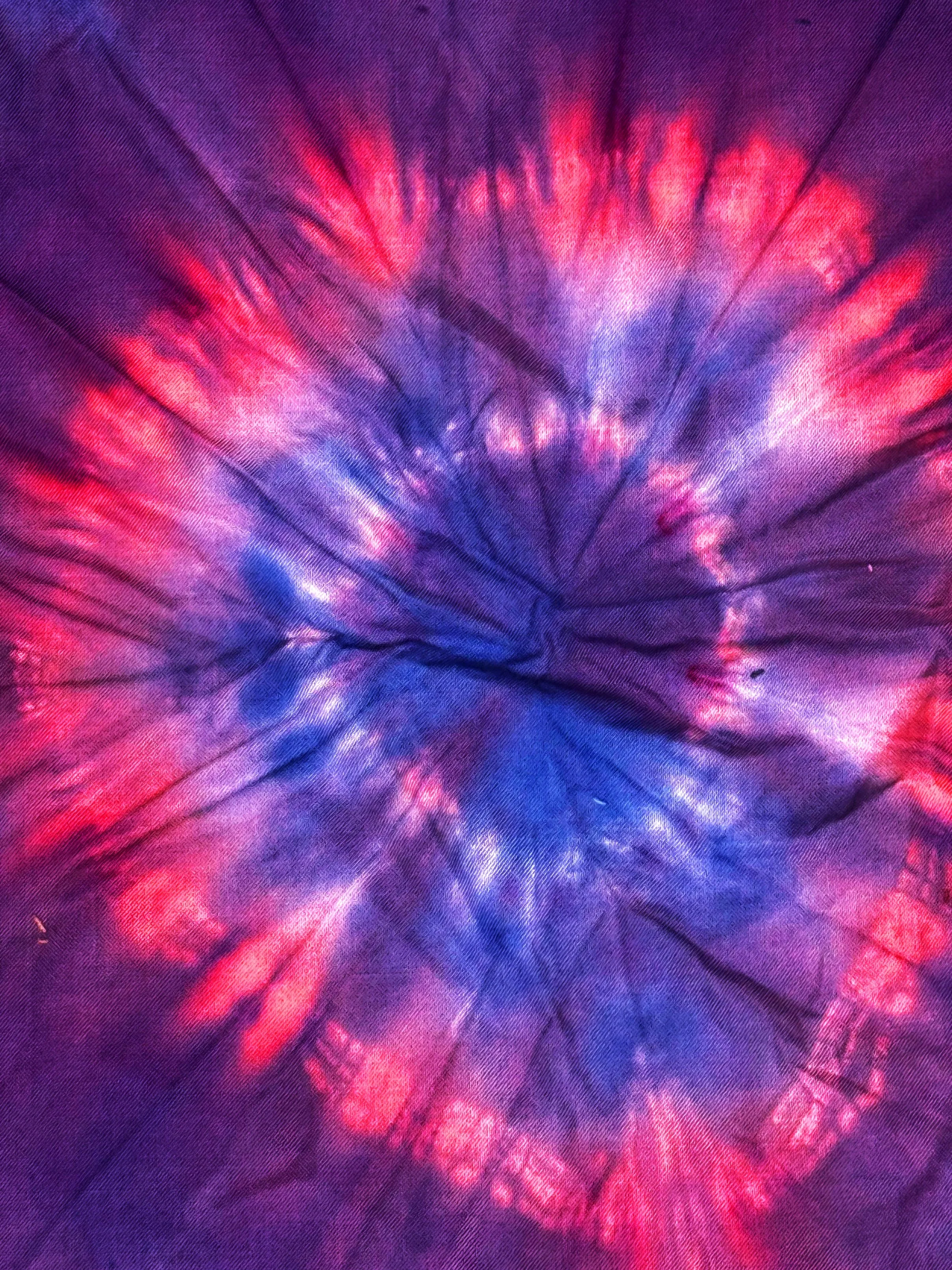 Close-up of a colorful tie-dye fabric with purple, blue, and pink hues arranged in a spiral pattern.