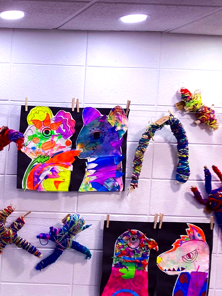 Colorful children's artwork and crafts displayed on a wall, including paper animal cutouts and wrapped pipe cleaner figures.