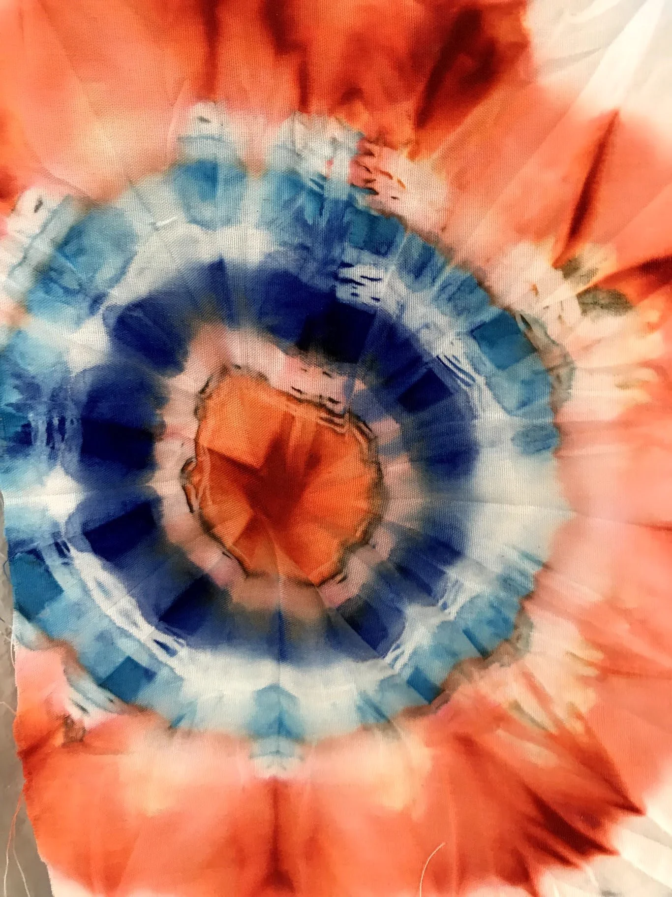 Close-up of a colorful, spiraled tie-dye fabric with orange, blue, and white patterns.