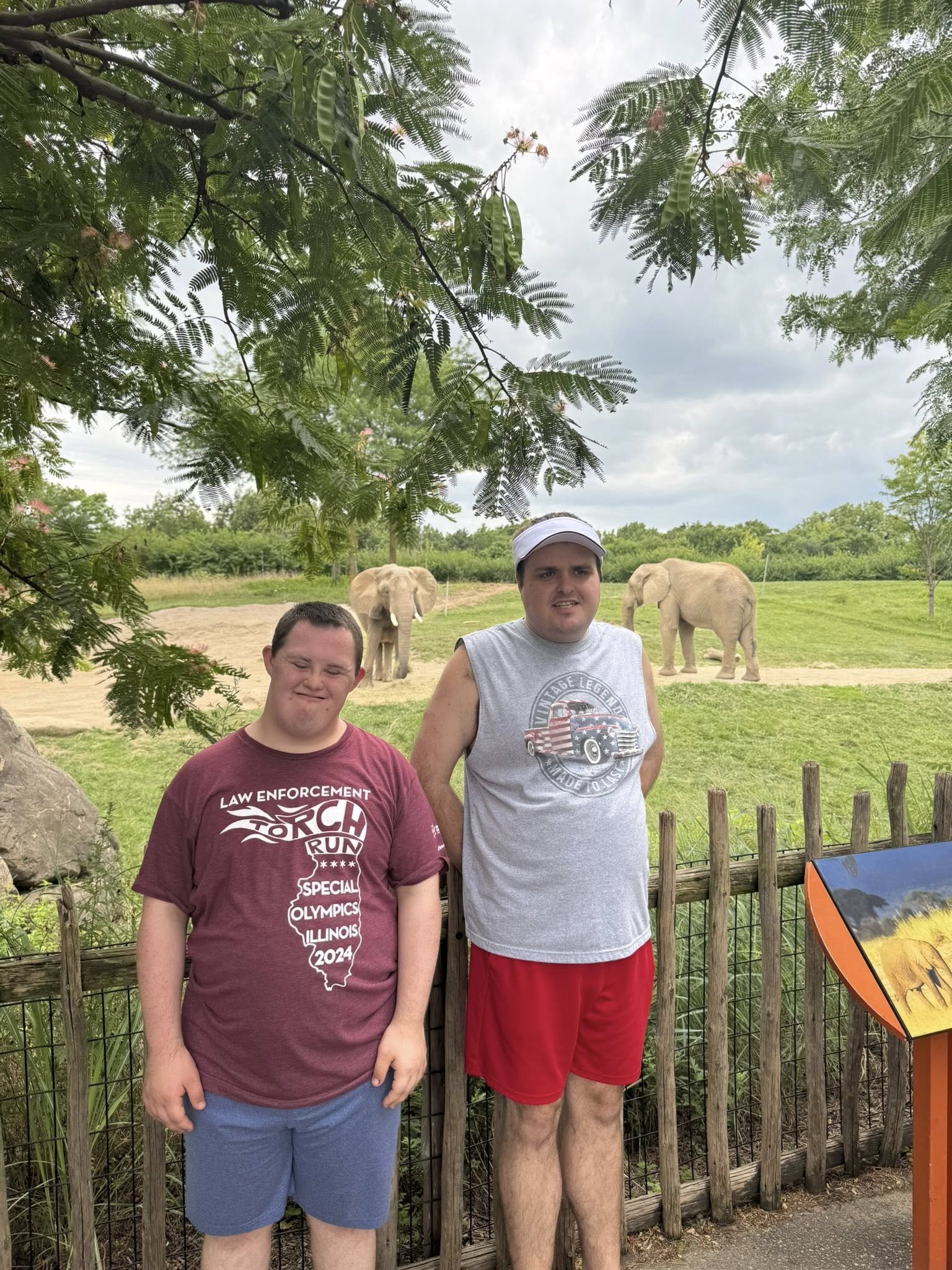 Jack and Chance smiling together at the zoo with elephants in the background.