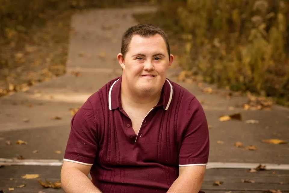 Chance smiling outdoors in a park during his senior photo session.